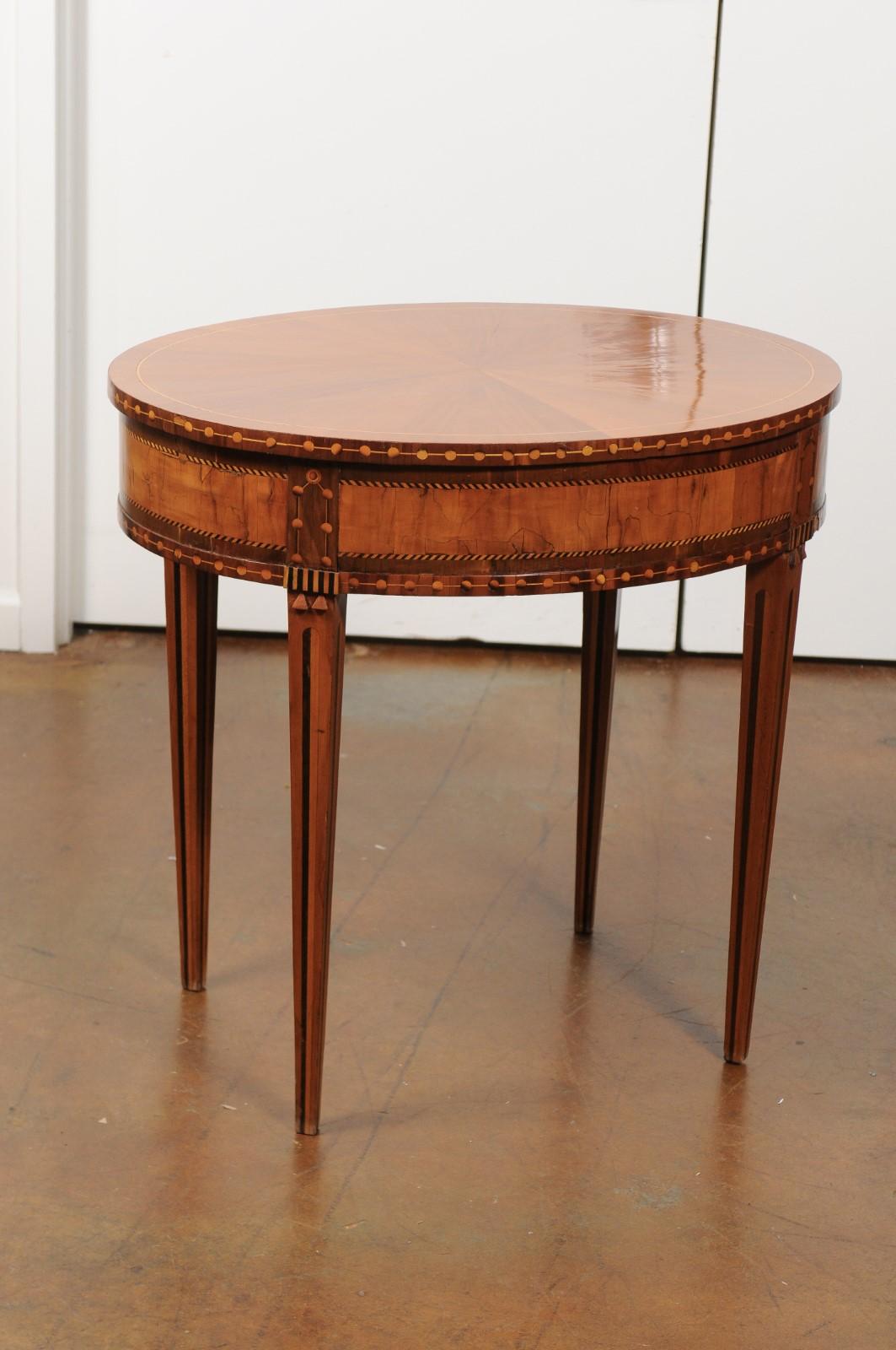 A French oval walnut and satinwood side table from the 19th century, with inlaid accents, radiating veneer and tapered legs. Born in France during the ever-changing 19th century, this French table features an oval top, adorned with an exquisite