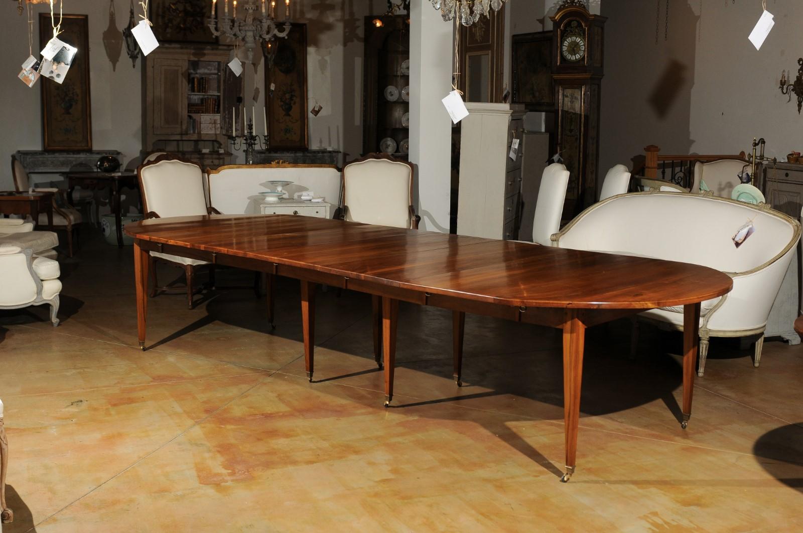 A French oval walnut dining room extension table with five leaves from the 19th century with tapered legs and casters. This French dining room table features an exquisite walnut top presenting five leaves, resting on a rectangular apron. The