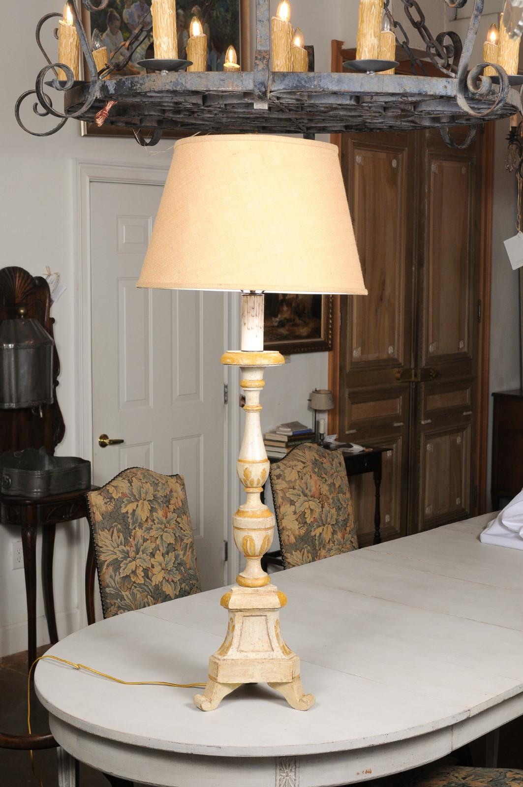 A French painted and carved candlestick from the 19th century, made into a table lamp with shade. Created in France during the 19th century, this candlestick features a turned column accented with painted foliage motifs. Resting on a tripod base