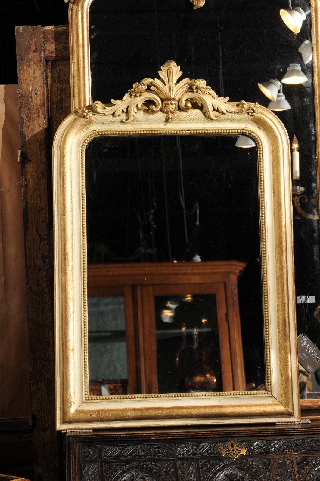 A French painted and parcel-gilt mirror from the 19th century, with acanthus leaf-carved crest and beads. This medium size French mirror features an elegant Louis-Philippe inspired frame, alternating painted and gilded accents. The mirror plate is