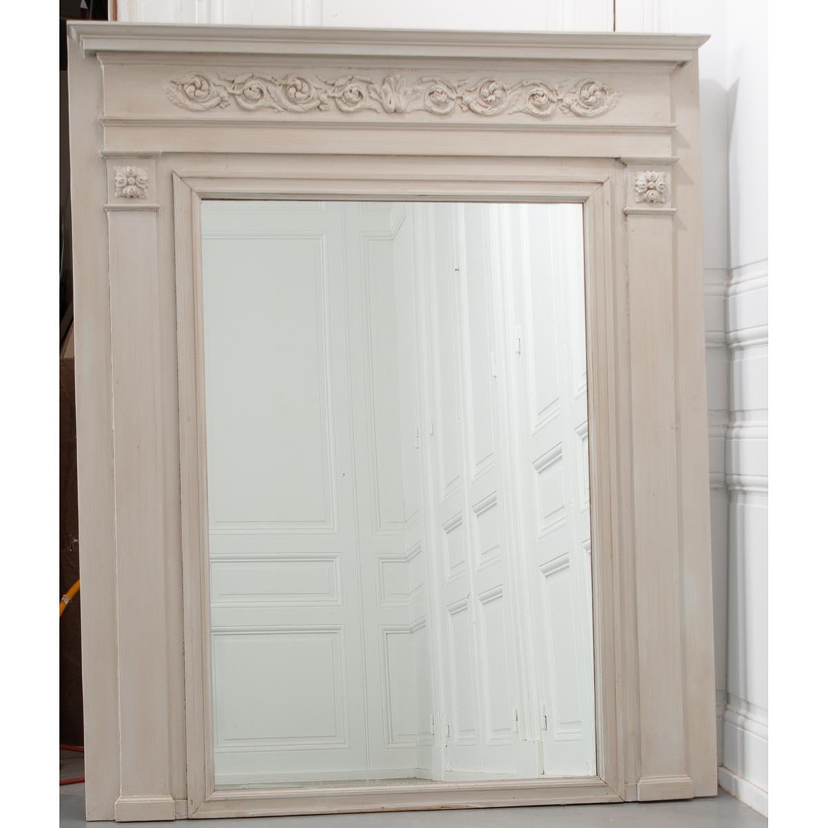 French, newly painted mirror of Boiserie from Rouen, France. This fine trumeau starts with a finished crown above a detailed scroll foliate pattern carved across the top of the mirror. The centered mirror plate has been replaced at some point and is