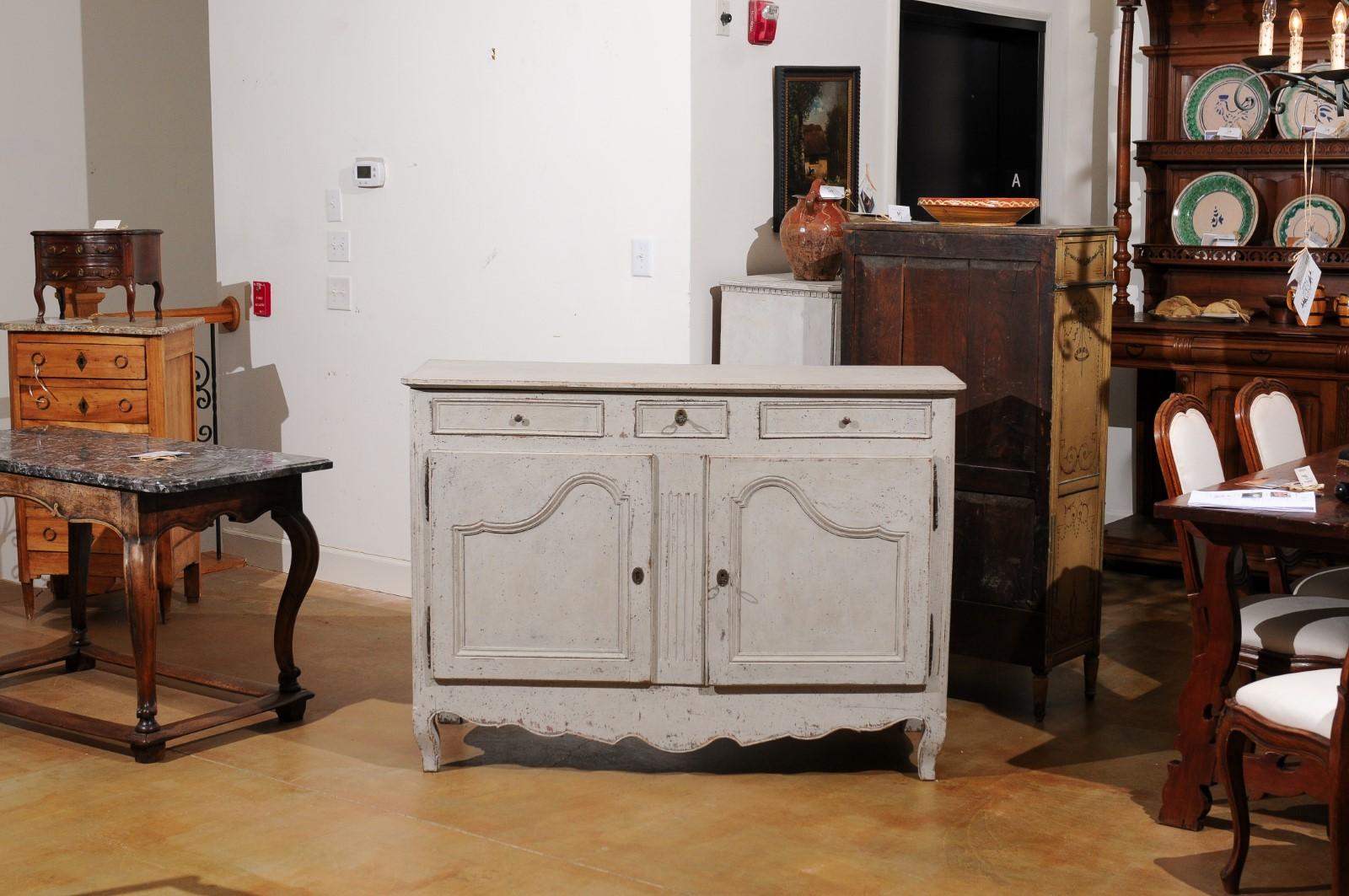 A French painted wood buffet from the 19th century, with three drawers, two doors, fluted accents and distressed finish. Created in France during the 19th century, this painted buffet features a rectangular top with rounded corners in the front,