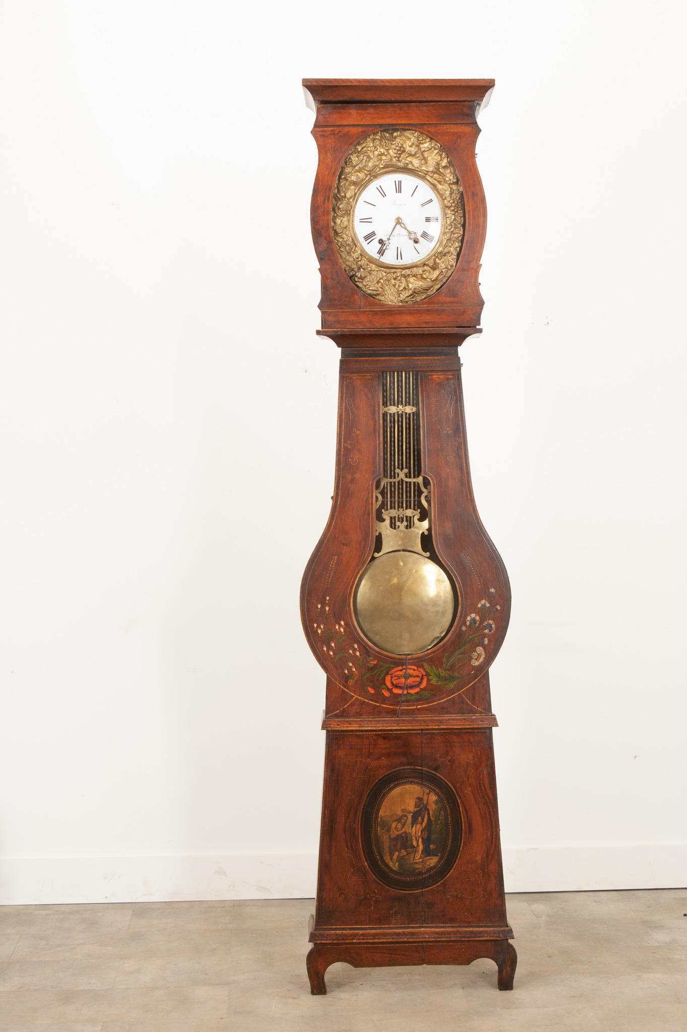 This French 19th Century banjo shaped case clock is an eye-catching piece in any space. Topped by a smartly carved cornice above the dial face door. Supported by an intricate brass repousse frontage, the dial face sports hand painted Roman numerals.