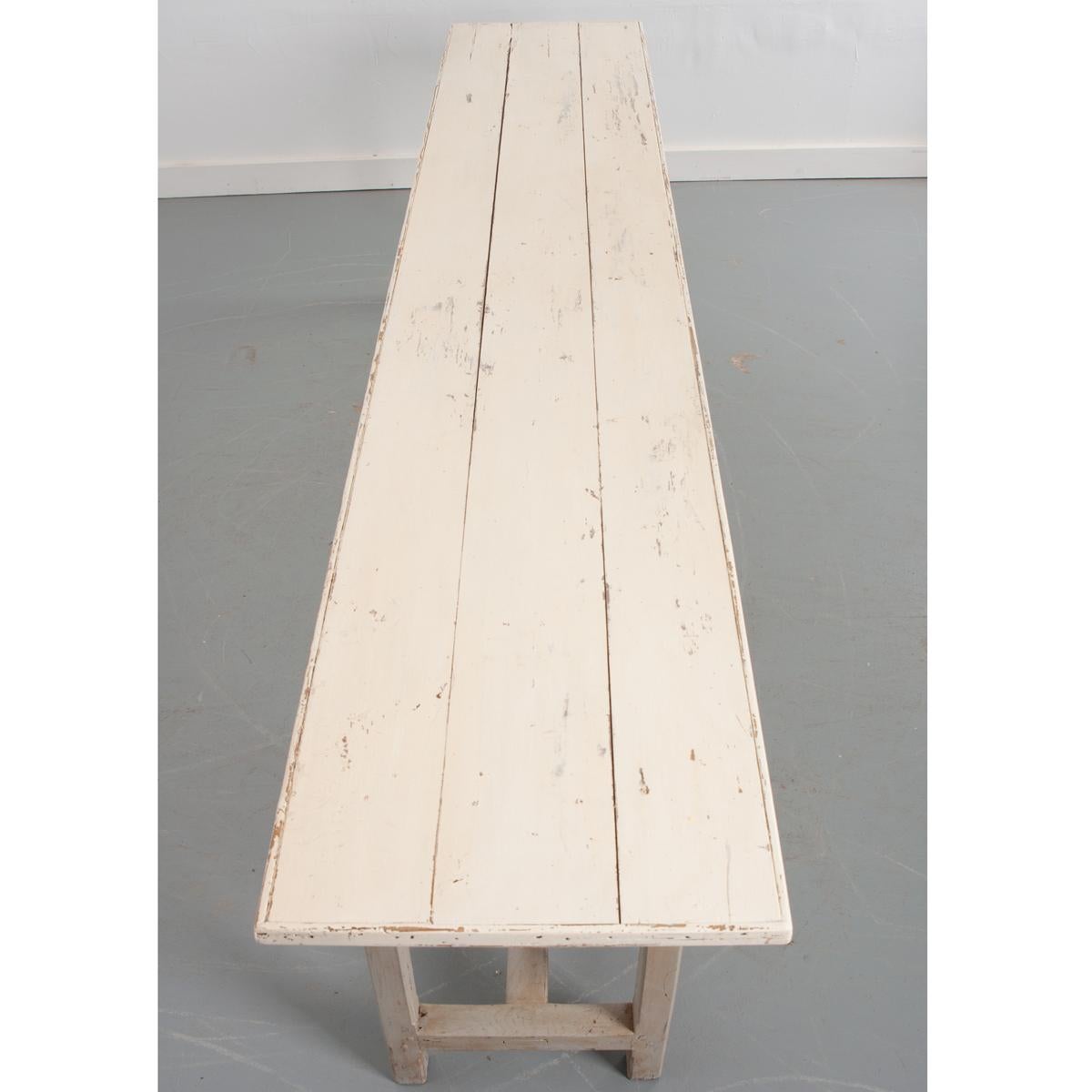 This long, narrow table is from France and is over nine feet long! It is from the 19th century, with recent paint. The top is off white and the base is light grayish-green. The legs are simple and straight with a ‘H’ shape stretcher connecting the