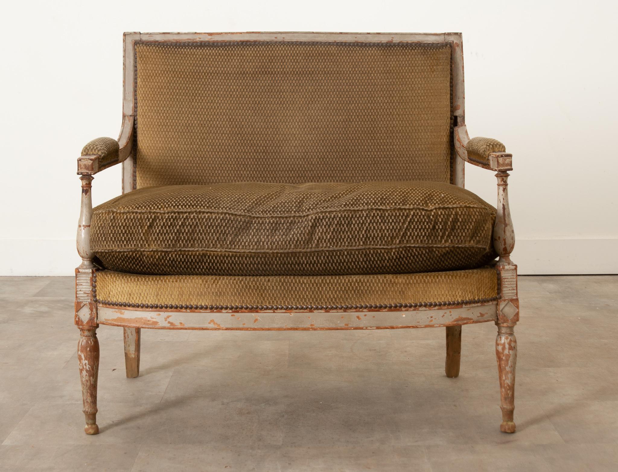 A French Directorie period petite settee is in wonderful antique condition. Hand carved and built in the early 1800’s, this settee is sturdy and is sure to bring a lot of character to your space. The carved wood frame boosts its original worn paint