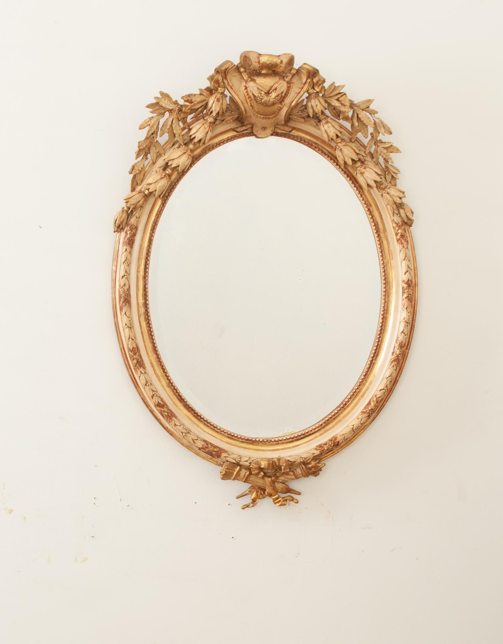 A circa 1840 French Louis XVI style gilt carved wood wall mirror crafted in 19th century France. The original beveled mercury mirror is in great condition and is surrounded by the handsome carved bead border of its cream-painted and water-gilt frame