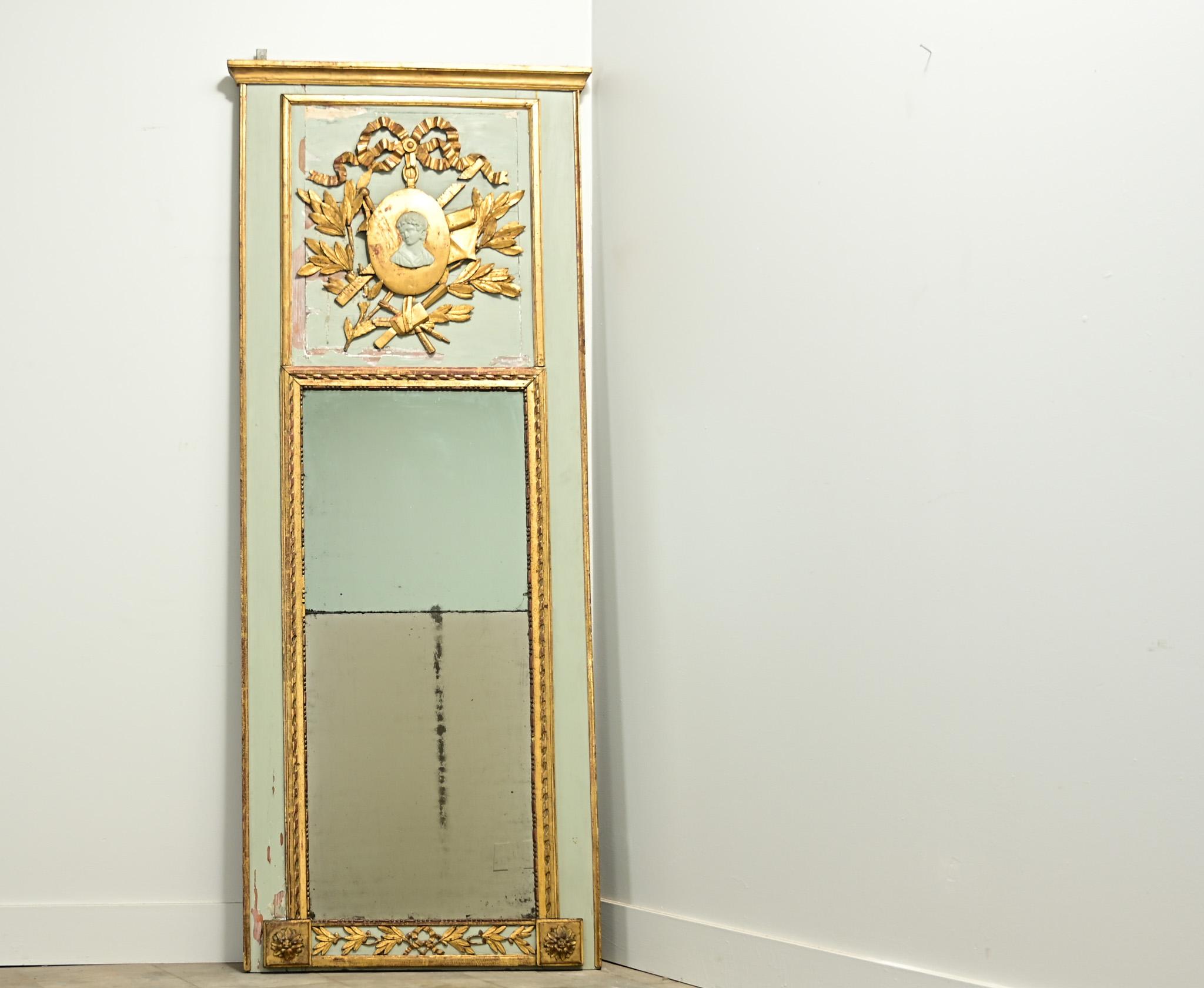 An interesting Empire style French trumeau taken from a larger boiserie paneling. The applied carved and gilt crest depicts a center cameo with bows, laurel leaves and architectural tools. The mirror plates are both old, however, not original to the