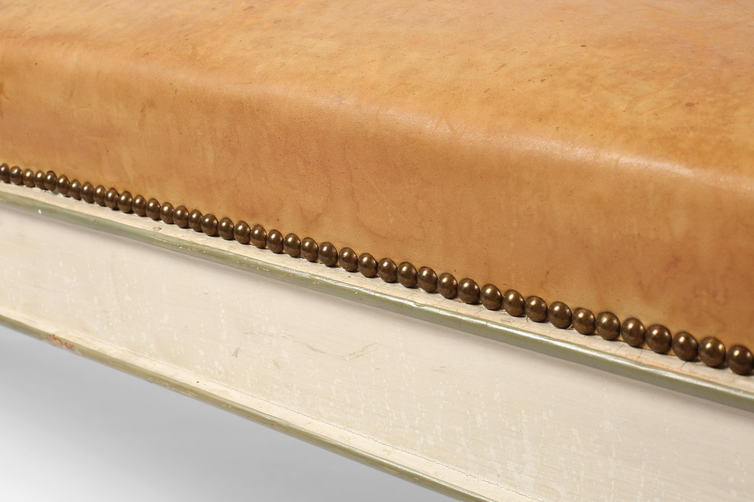 Una panca del XIX secolo affascinante e incredibilmente utile, rivestita in morbida pelle color caramello con finiture in ottone. La struttura in legno intagliato e tornito vanta la verniciatura originale in bianco sporco, con accenti e decorazioni