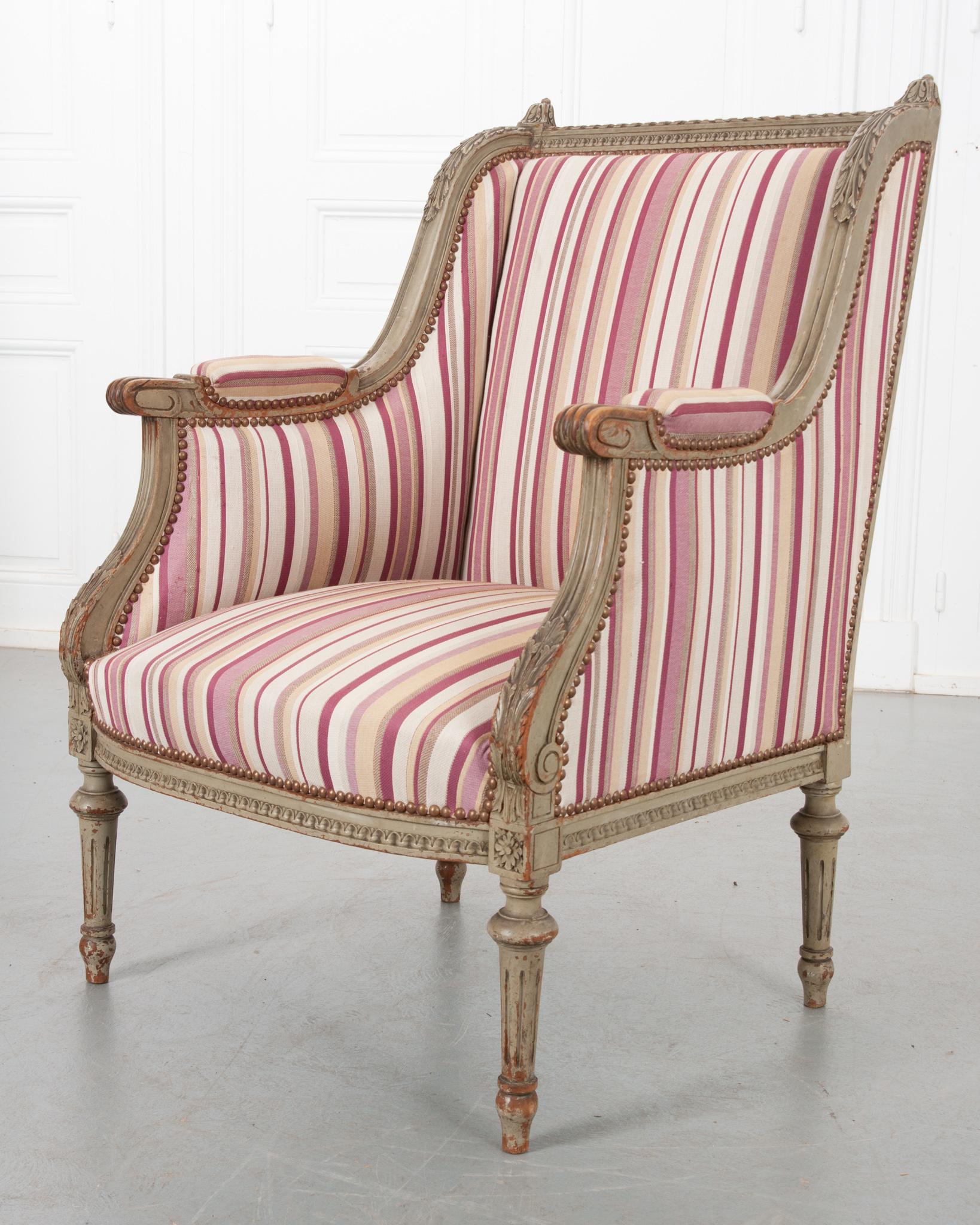 Une fabuleuse bergère individuelle de style Louis XVI du 19ème siècle en France. Ce fauteuil ancien présente une armature méticuleusement sculptée et peinte, sur laquelle un joli tissu à rayures a été apposé. Le cadre carré est orné de motifs