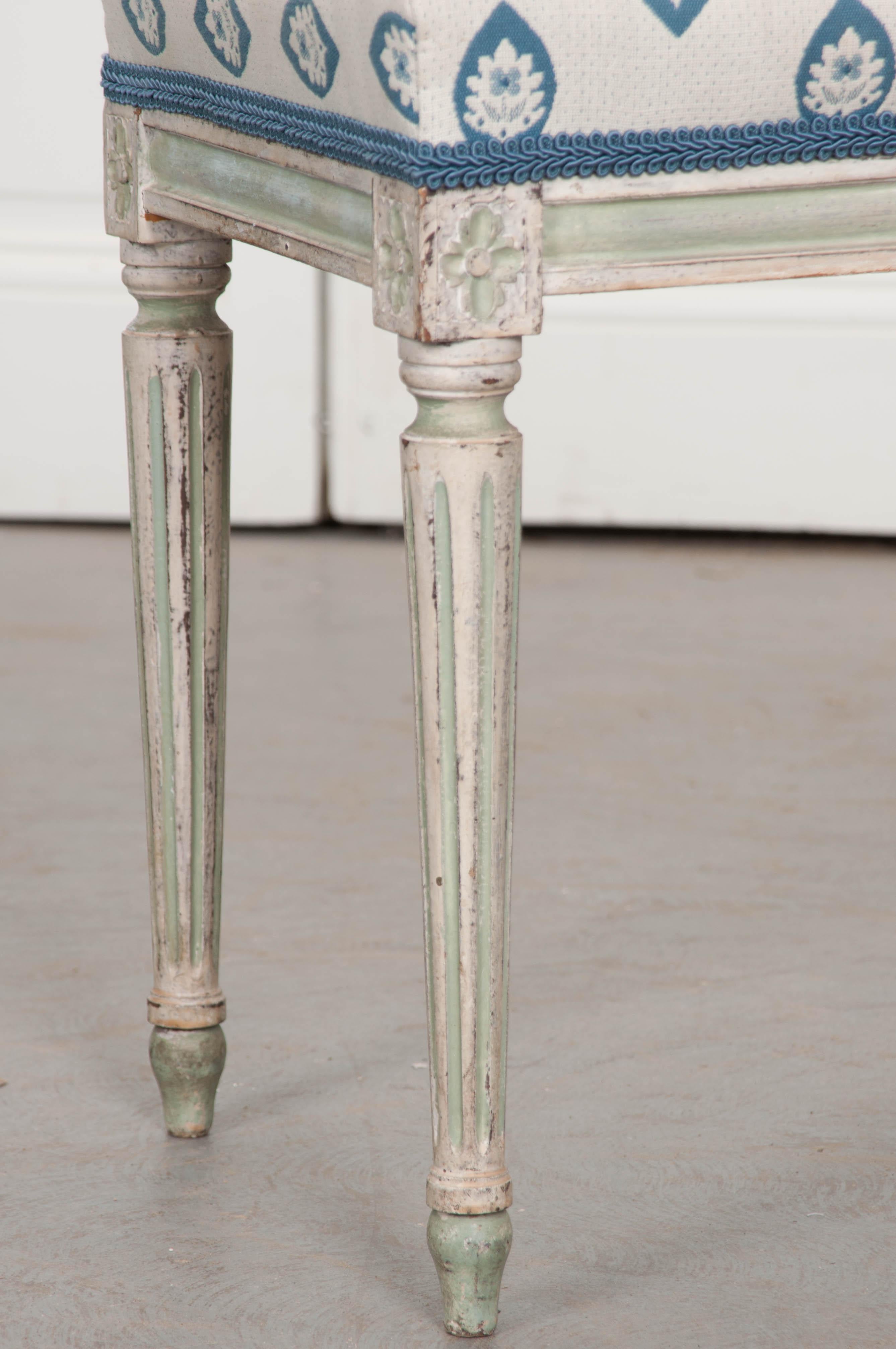 A darling painted Louis XVI style stool from the latter part of the 19th century. The stool is painted a lovely cream color with serene, powder blue-painted accents. The frame is quintessentially Louis XVI, with rosette-carved joinery dies and