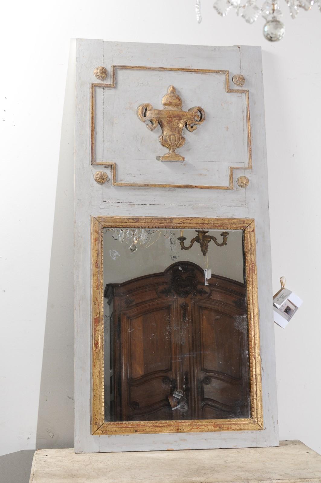 A French painted trumeau mirror from the 19th century, with carved giltwood vase and mercury glass. Born in France during the politically dynamic 19th century, this trumeau mirror features a rectangular light grey painted frame, accented with a