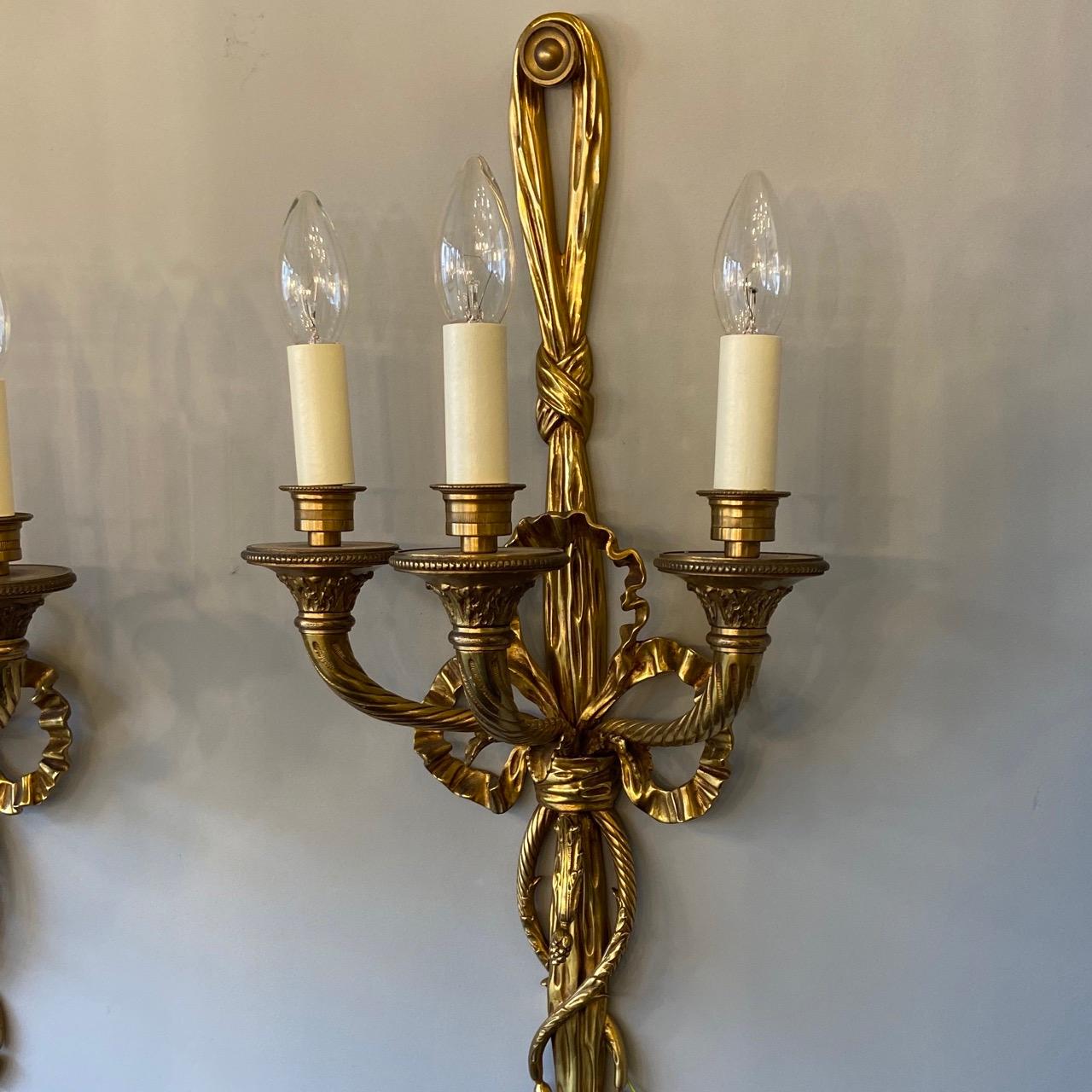 A quality French pair of gilded bronze triple arm antique wall lights, the barley twisted scrolling arms with leaf clad trumpet millgrain bobeche drip pans and candle sconces, issuing from a decoratively cast elongated rope and tassel pierced