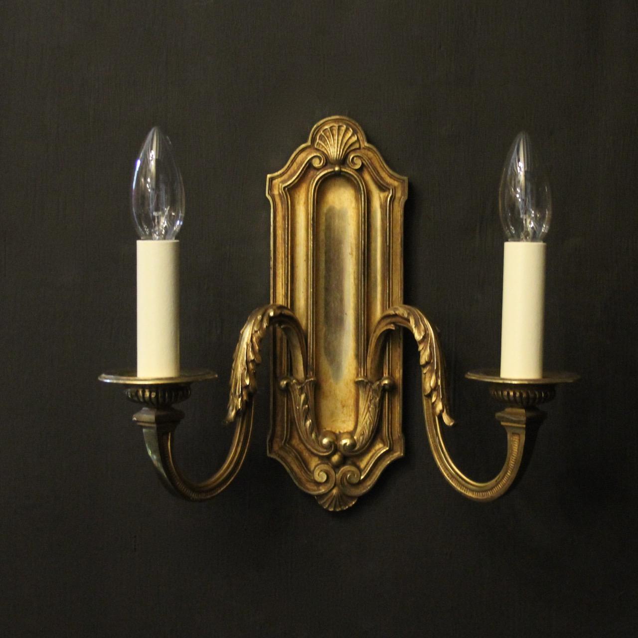 A French pair of gilded bronze twin arm antique wall lights, the leaf clad square gauge scrolling arms with sectional reeded bobeche drip pans, issuing from an rectangular leaf backplate with scallop shell finial, nice original gilded patination and