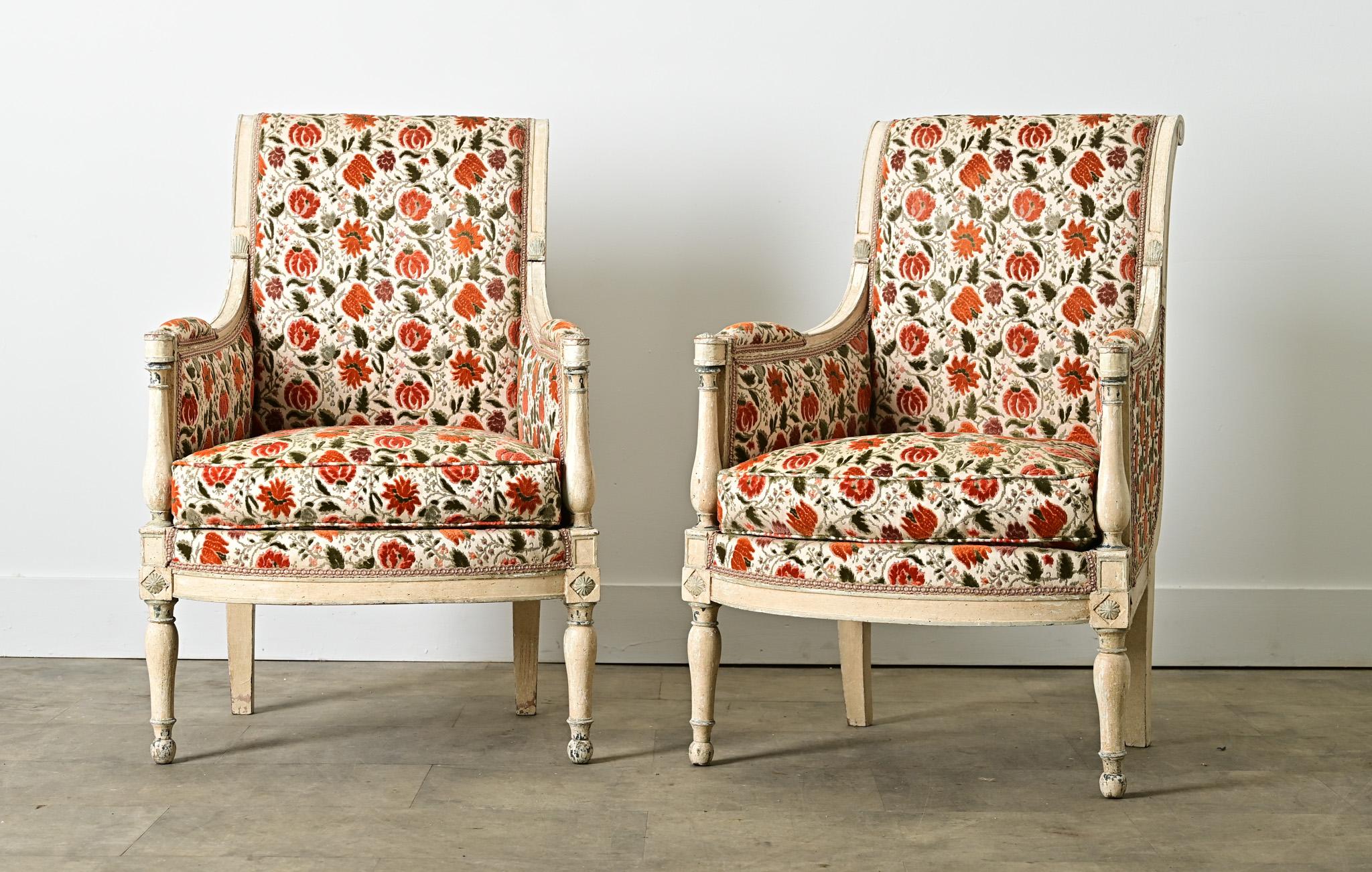 Une paire accueillante de chaises bergères françaises du 19ème siècle, fabriquées dans le goût Directoire avec des influences de Louis XVI pour un attrait intemporel. La paire est caractérisée par un magnifique velours coupé de motifs floraux corail
