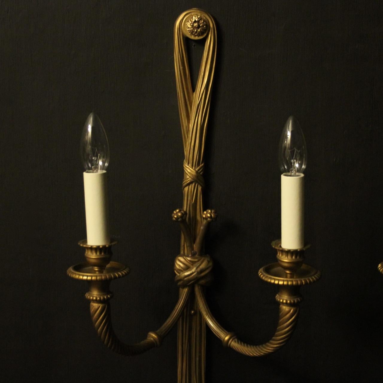 A large French pair of gilded bronze twin arm antique wall lights, the barley twisted scrolling arms with trumpet millgrain bobeche drip pans and sectional candle sconces, issuing from a decoratively cast elongated rope and tassel pierced backplate