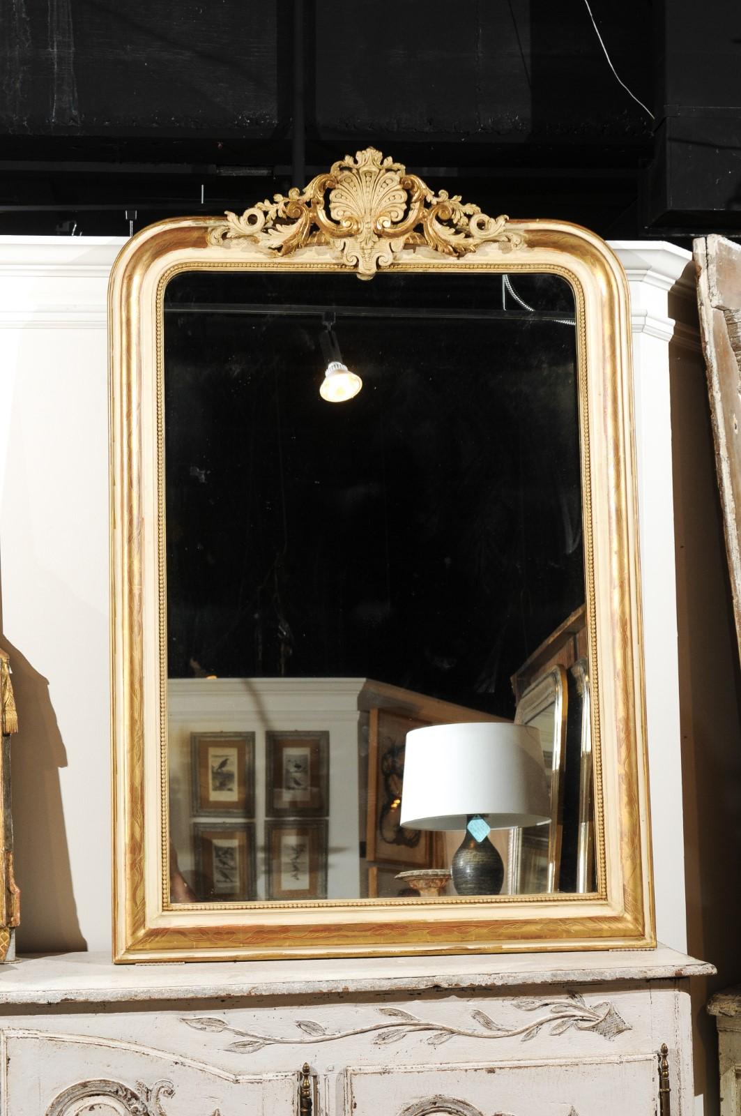A French parcel-gilt and hand-painted carved mirror from the 19th century with shell, foliage and bead motifs. This French wall mirror features an exquisite carved crest, adorned with a central shell accented with petite beads, flanked with