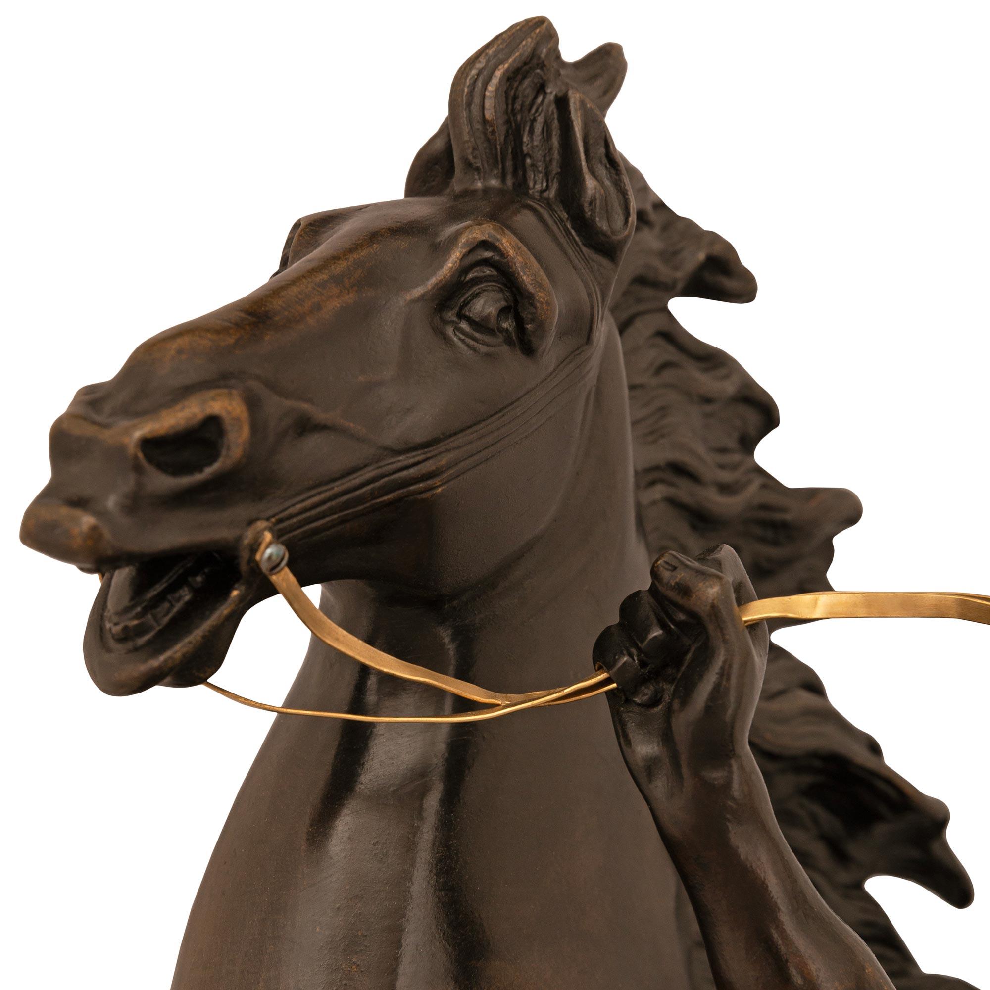 An impressive and majestic French 19th century patinated Bronze and Ormolu statue of a horse and groom, modeled after the horses of Marly. The spectacular horse is draped in a saddle blanket and displays a wonderful flowing mane and tail while