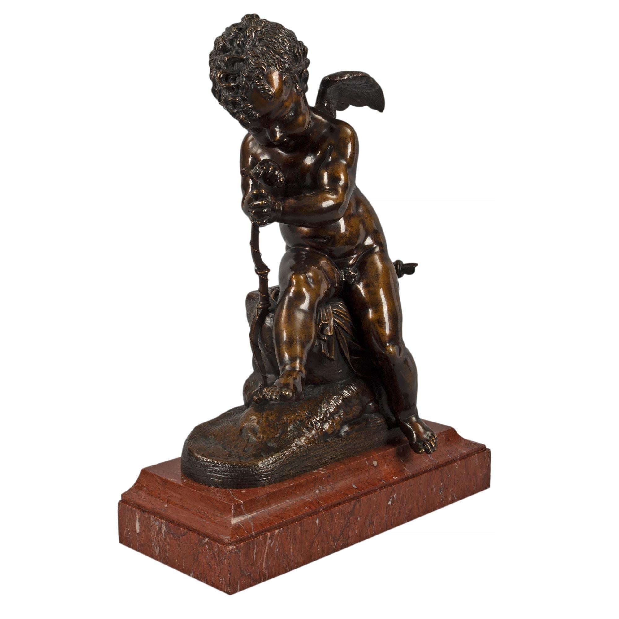 A charming and very elegant French mid 19th Century patinated bronze statue of a cherub, after Charles Gabriel Lemire. The statue is raised by a rectangular Rouge Griotte marble base with a concave top mottled border. Above is a sweet winged cherub,