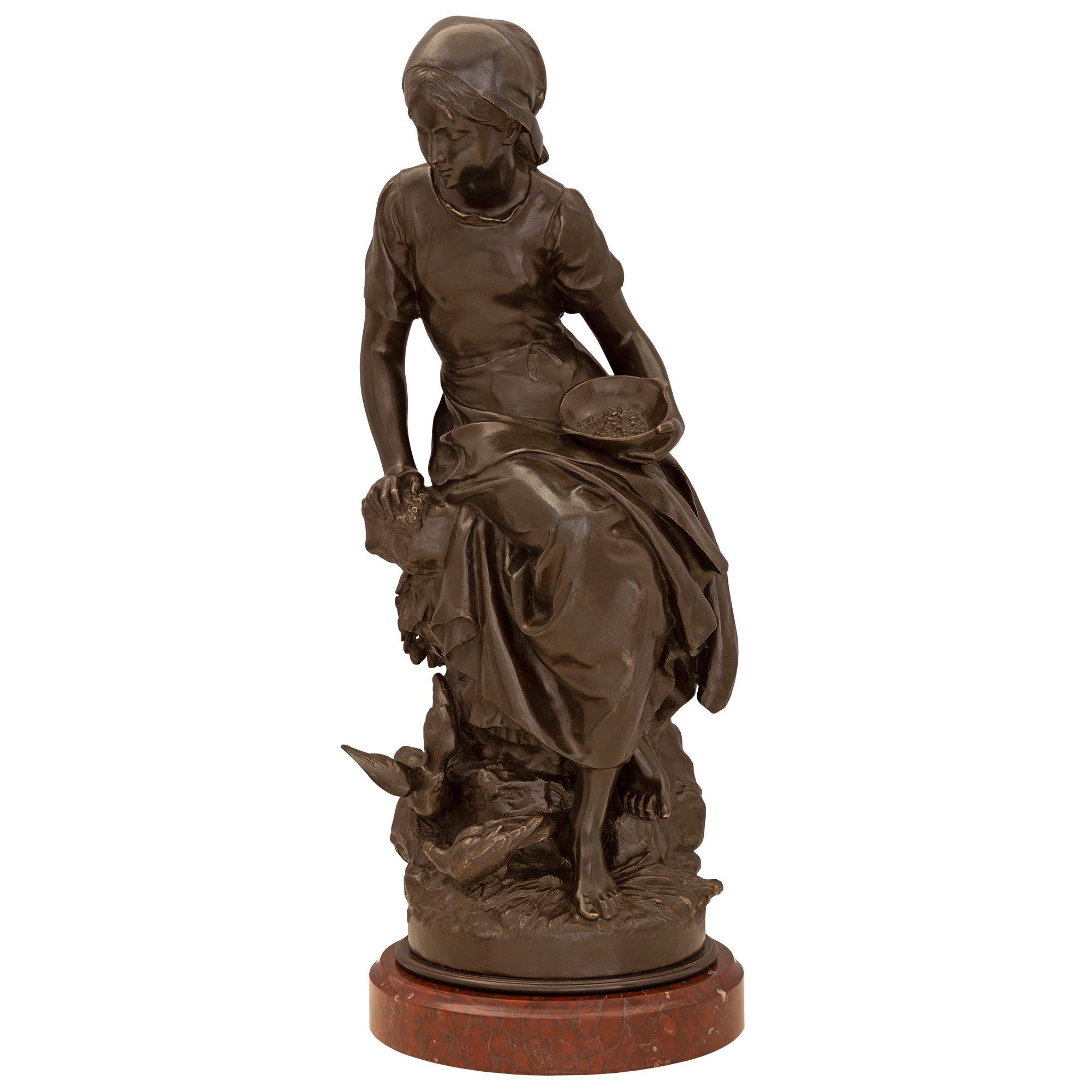 A charming high quality French 19th century patinated bronze statue named 'Paysanne nourrissant des oiseaux', by Mathurin Moreau. The elegant statue is raised by a circular mottled Rouge Griotte marble base below a finely detailed terrain designed