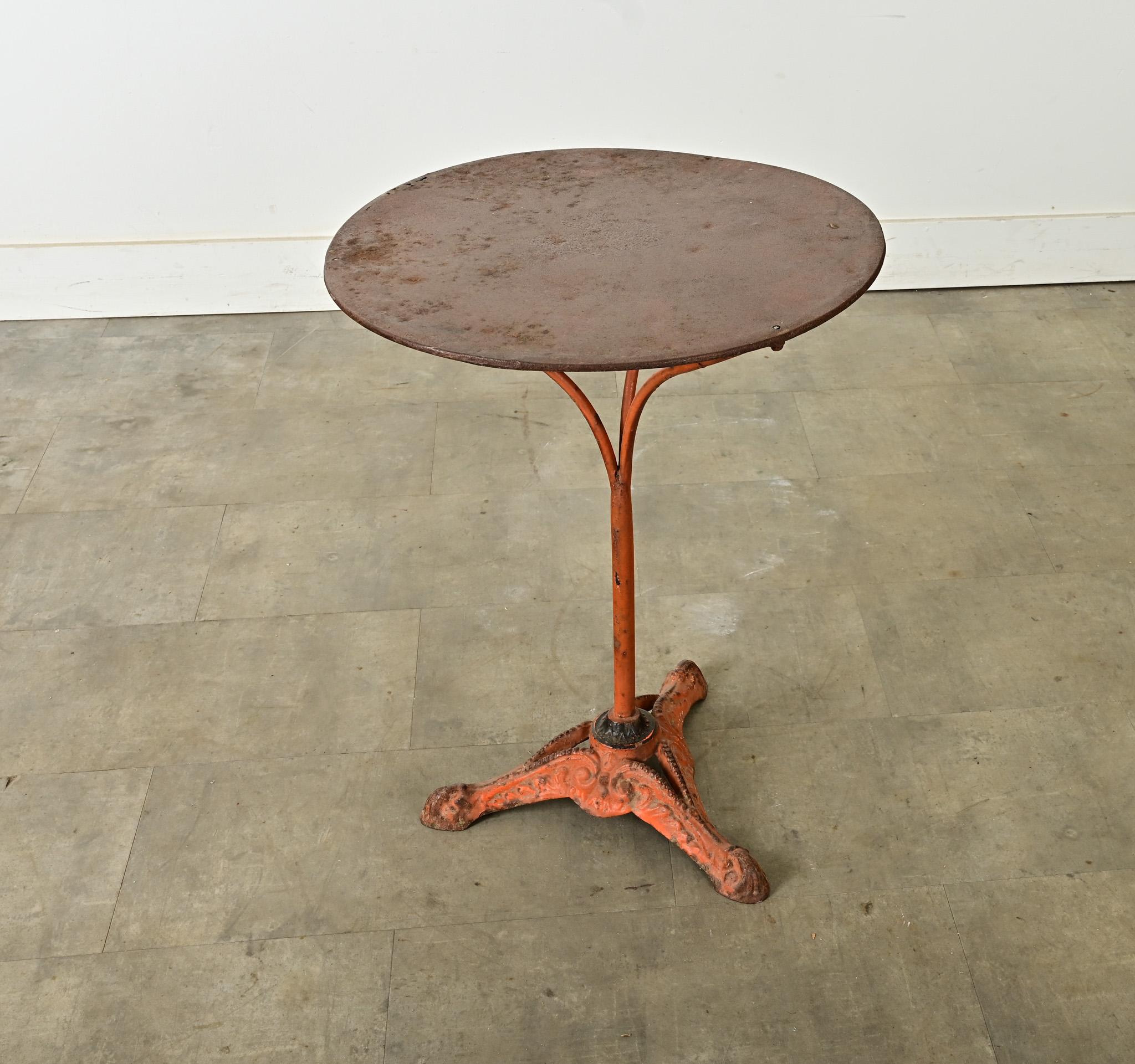 Tavolo da bistrot rotondo in ghisa francese di inizio secolo (circa 1900) con patina rovinata dalle intemperie che corrisponde a ciò che resta della vernice originale color terracotta-arancio. La superficie metallica circolare del piano del tavolo,