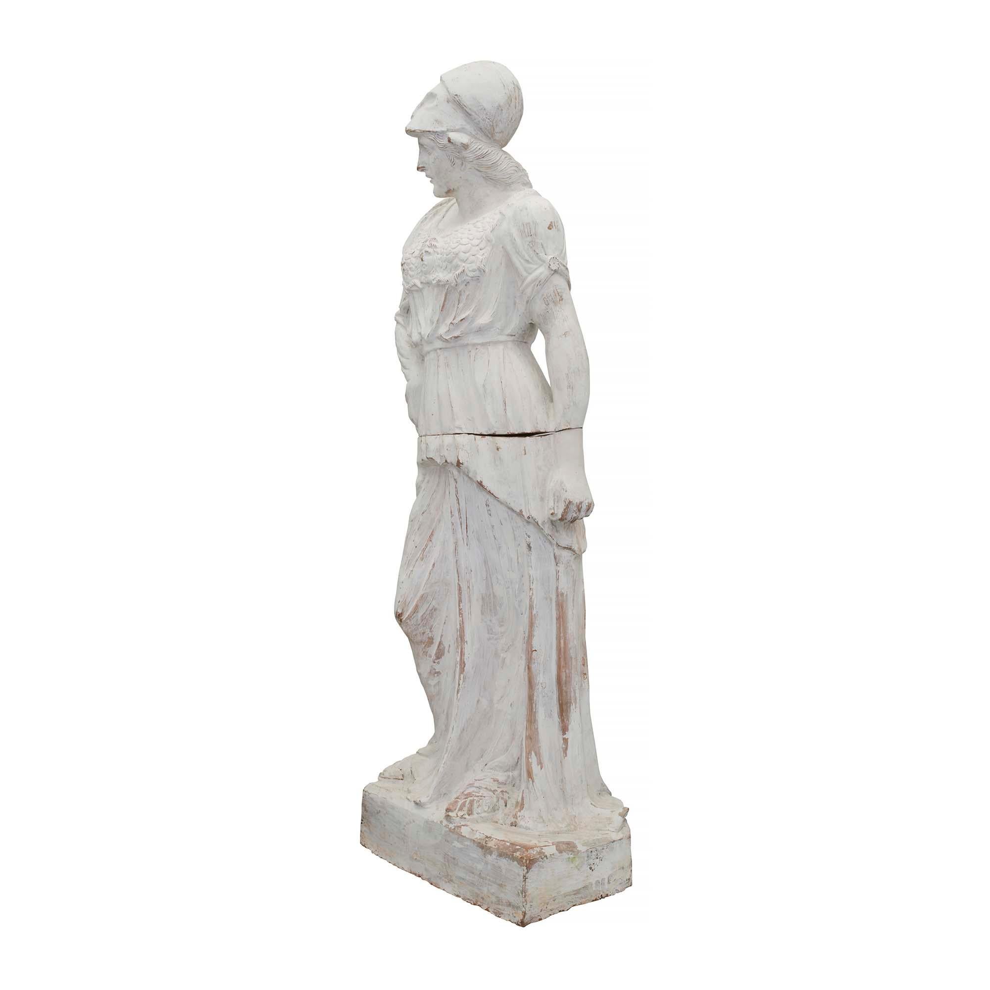 Belle statue de jeune fille en terre cuite patinée du XIXe siècle. La statue en deux parties est surélevée par une base rectangulaire où se tient la jeune fille. Elle porte des sandales et est drapée dans des vêtements d'époque. À travers sa tenue,