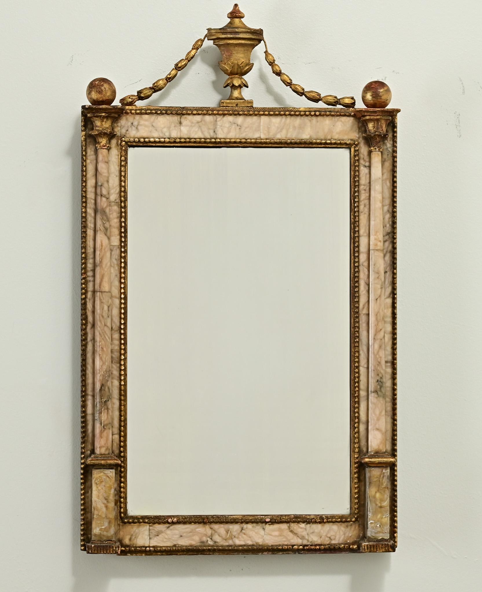 A petite and unique alabaster mirror from 19th Century France. The top features a gold gilt urn with garland and ball finials. The carved and applied alabaster mirror frame has a beaded brass trim and alabaster columns. Be sure to view the detailed