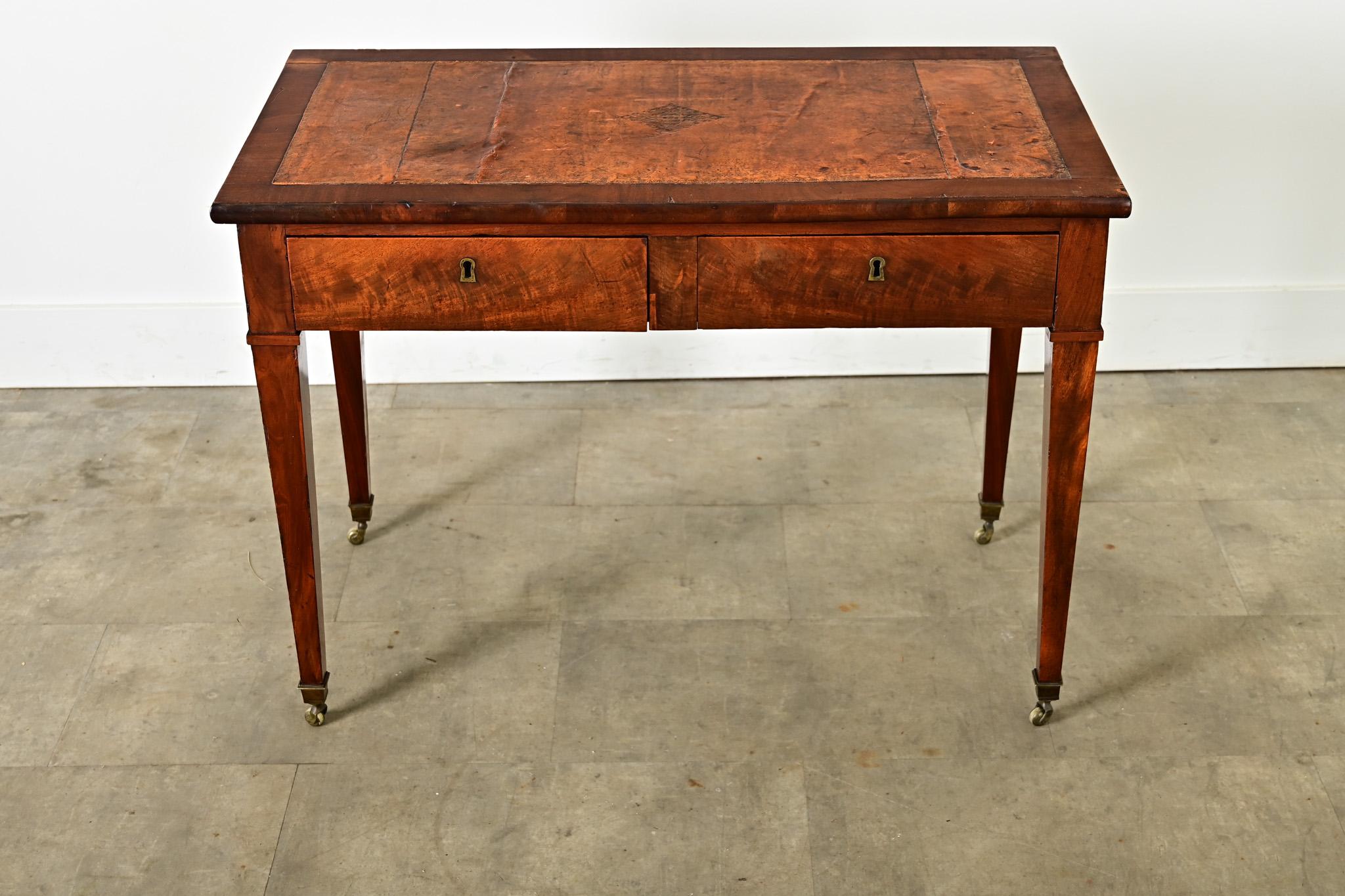 A petite, French occasional table or writing desk from the 19th century with a very well-patinated leather surface in a gorgeous mahogany frame. The Directoire silhouette of this handsome desk celebrates the strength of refined proportions and