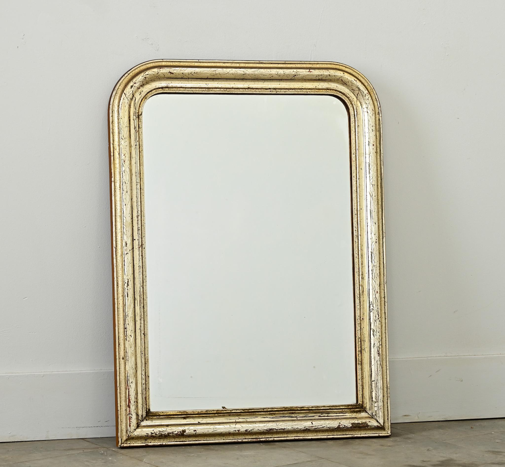 Miroir Louis Philippe français du XIXe siècle, de taille modeste, avec un motif de feuillage légèrement sculpté dans le cadre arqué et doré, rehaussé par une oxydation foncée et une texture craquelée. A noter quelques fissures et usures qui donnent