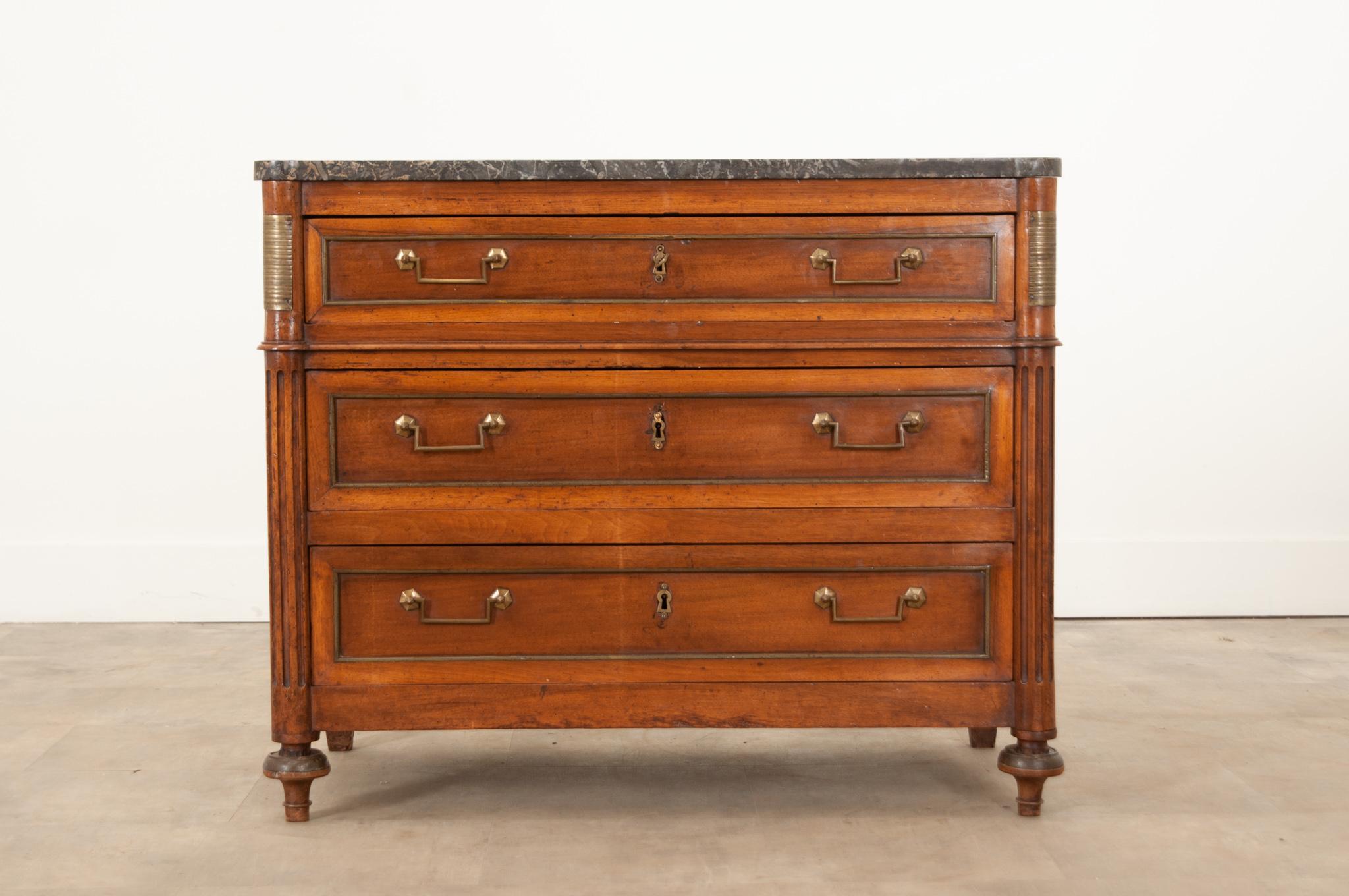 A petite 19th Century Louis XVI style commode hand-crafted in France circa 1860. This stylish case piece is made of mahogany and topped with its original, removable, shaped marble top that has incredibly gorgeous gray patterns throughout. A bank of