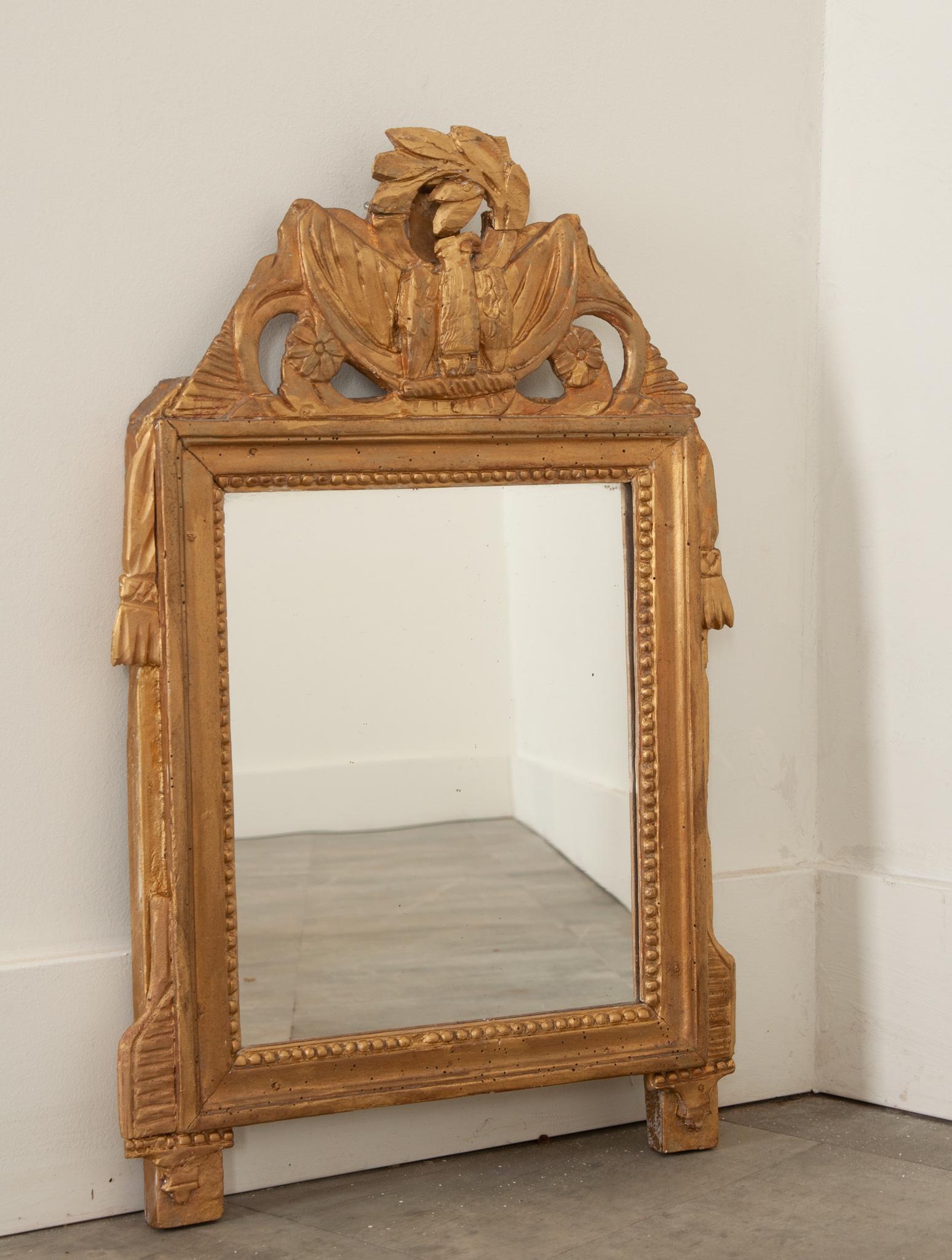 A darling petite mirror from France created in the 19th century that would be perfect in a powder or dressing room. An eagle crowned with laurel perches atop the whole with drapery swags down the sides. The original mirror plate is in great antique