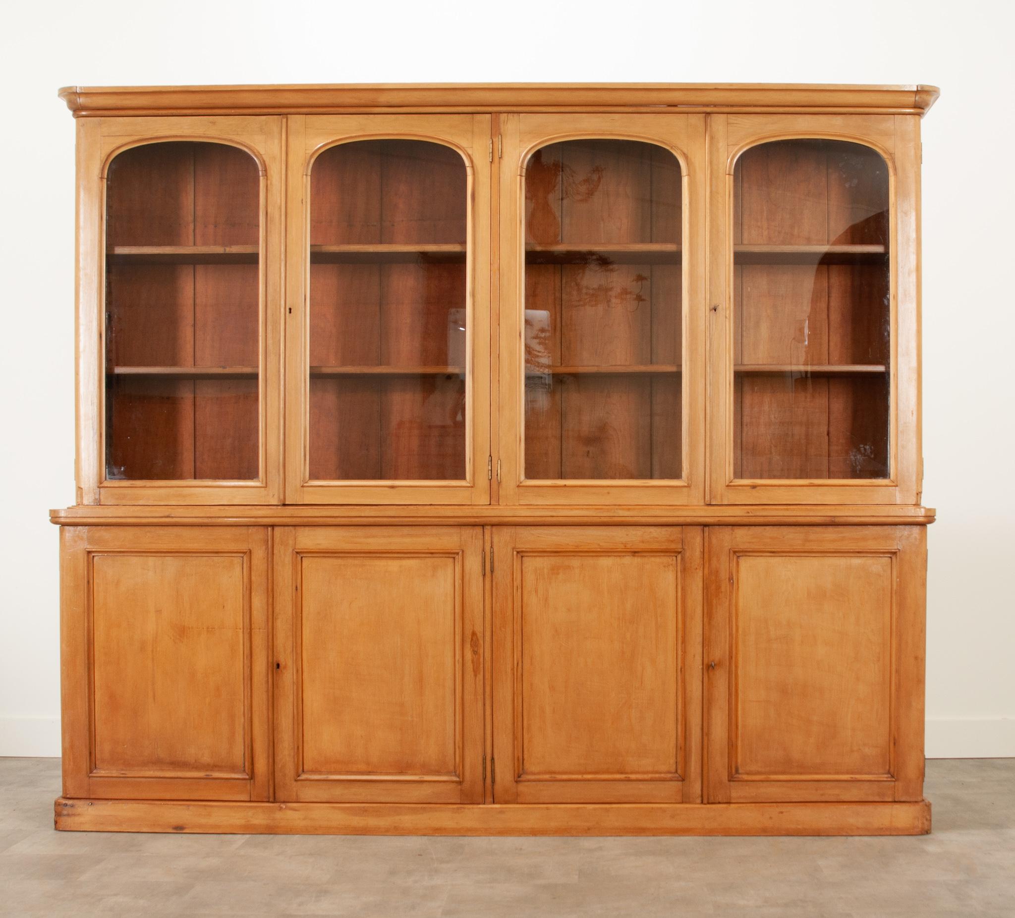 A sizable pine bibliotheque crafted in France circa 1860. The four arched glass front, locking and latching upper doors close before two saw-tooth adjustable shelves diverge in the center of the piece. Four lower doors close before two separate