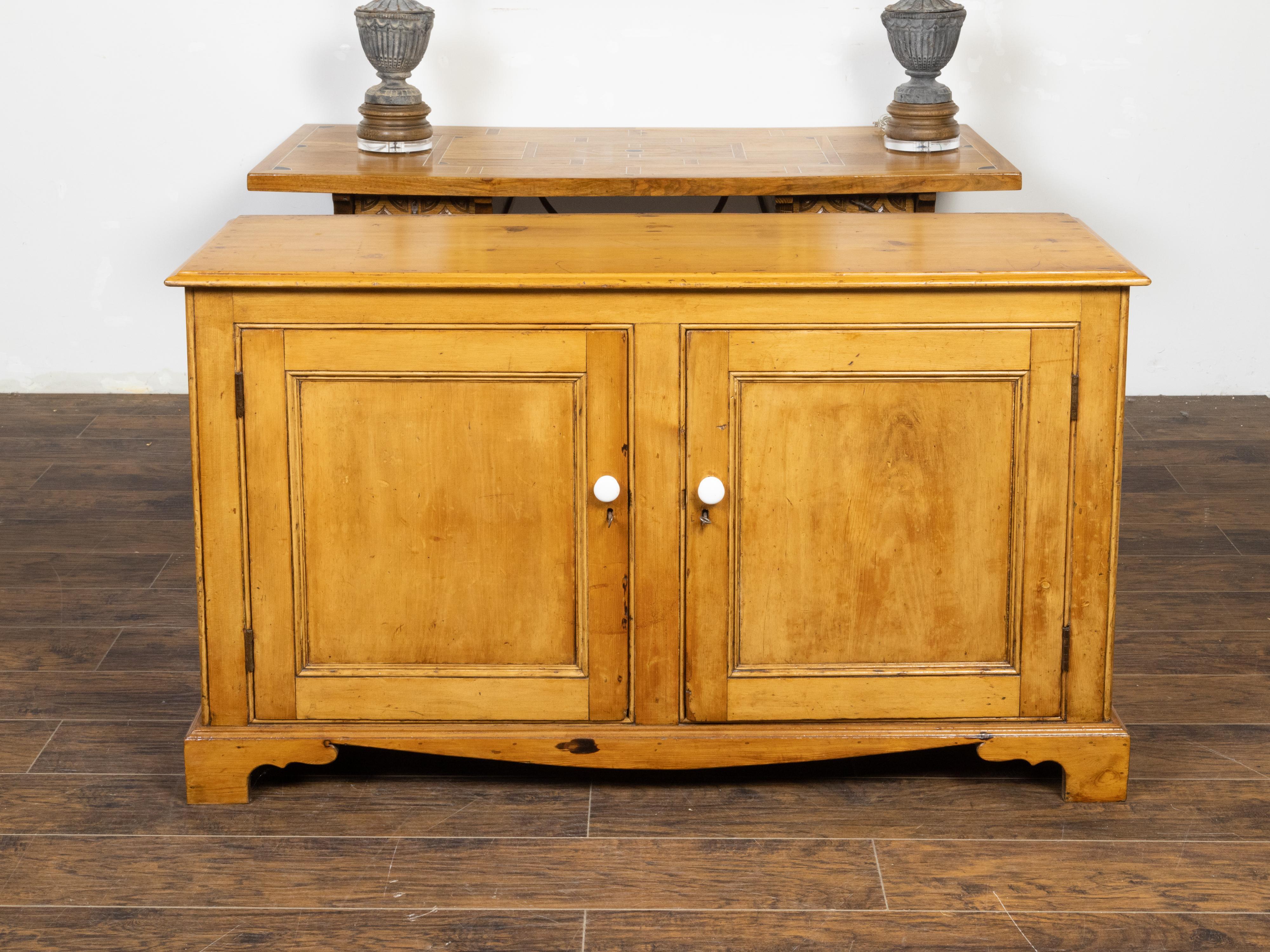 A French pine buffet from the 19th century, with two doors, carved ogee bracket feet, white pulls and nice patina. Created in France during the 19th century, this pine buffet features a rectangular top with beveled edges, sitting above two simple
