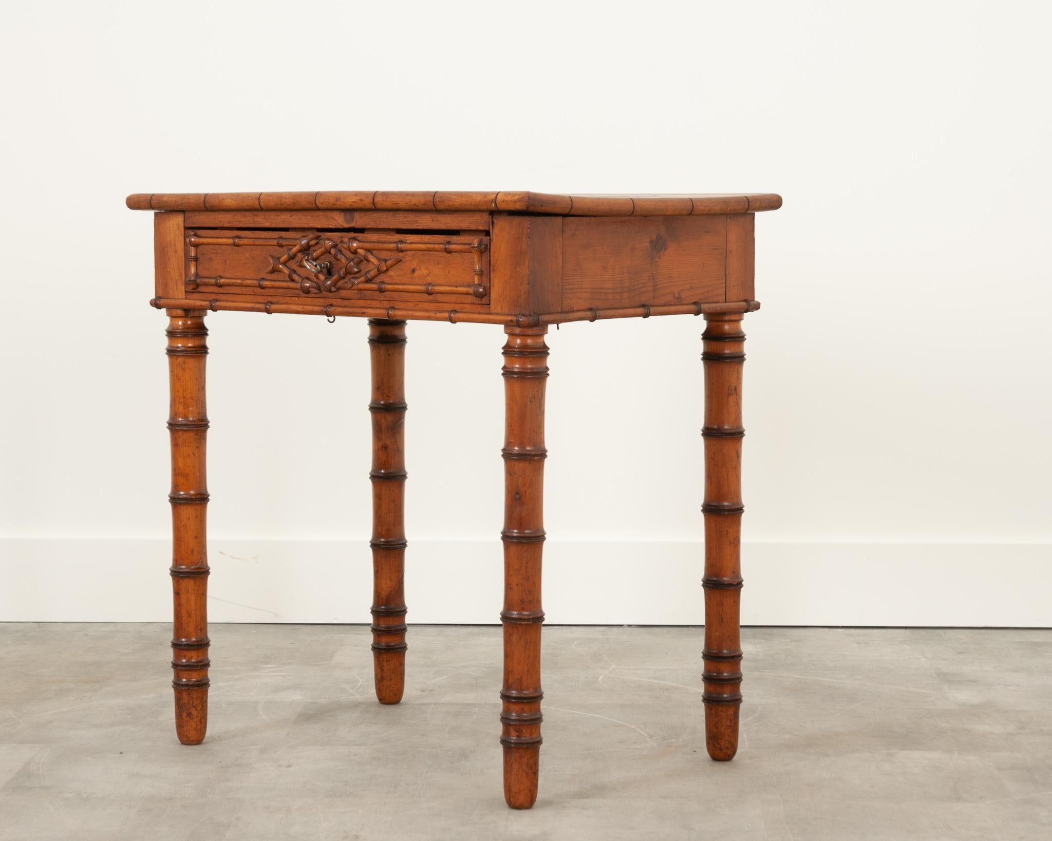 This funky, faux bamboo table was crafted in France during the 19th century. The vibrant pine has a fantastic patina throughout. The apron houses a single drawer with a criss-cross faux bamboo carved design. One key is included for the functional
