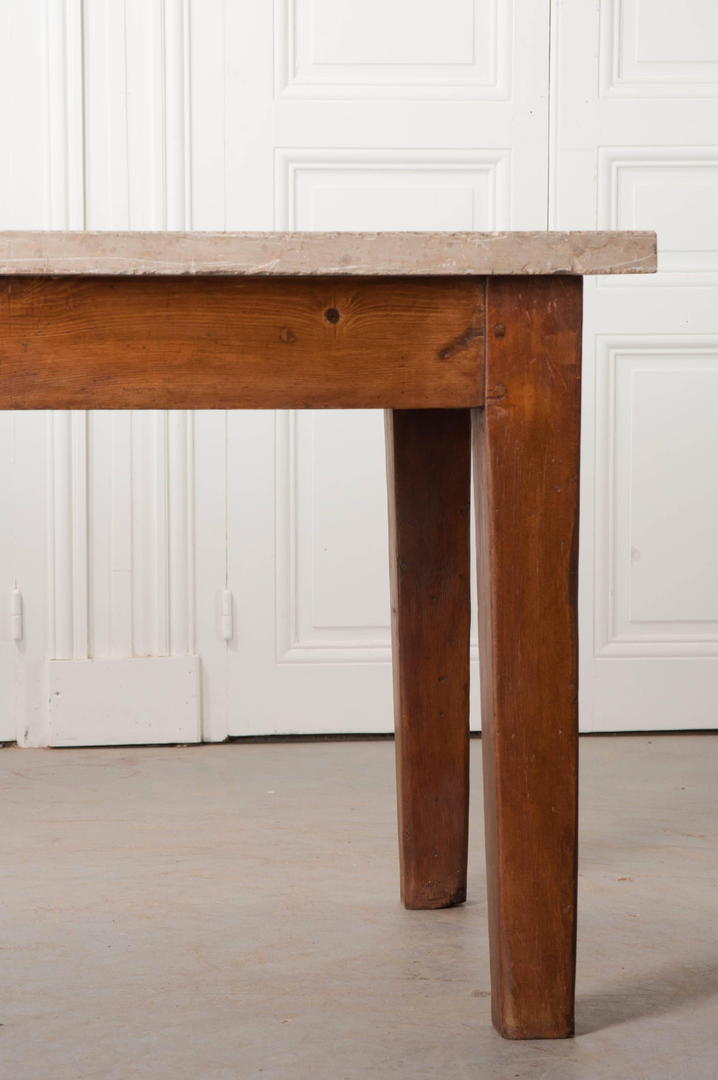This hefty table comes from France, and was made towards the end of the 19th century. The table’s top is a large, thick slab of taupe-colored limestone that has been polished, with the edges left somewhat live. It is held up by a solid-pine base