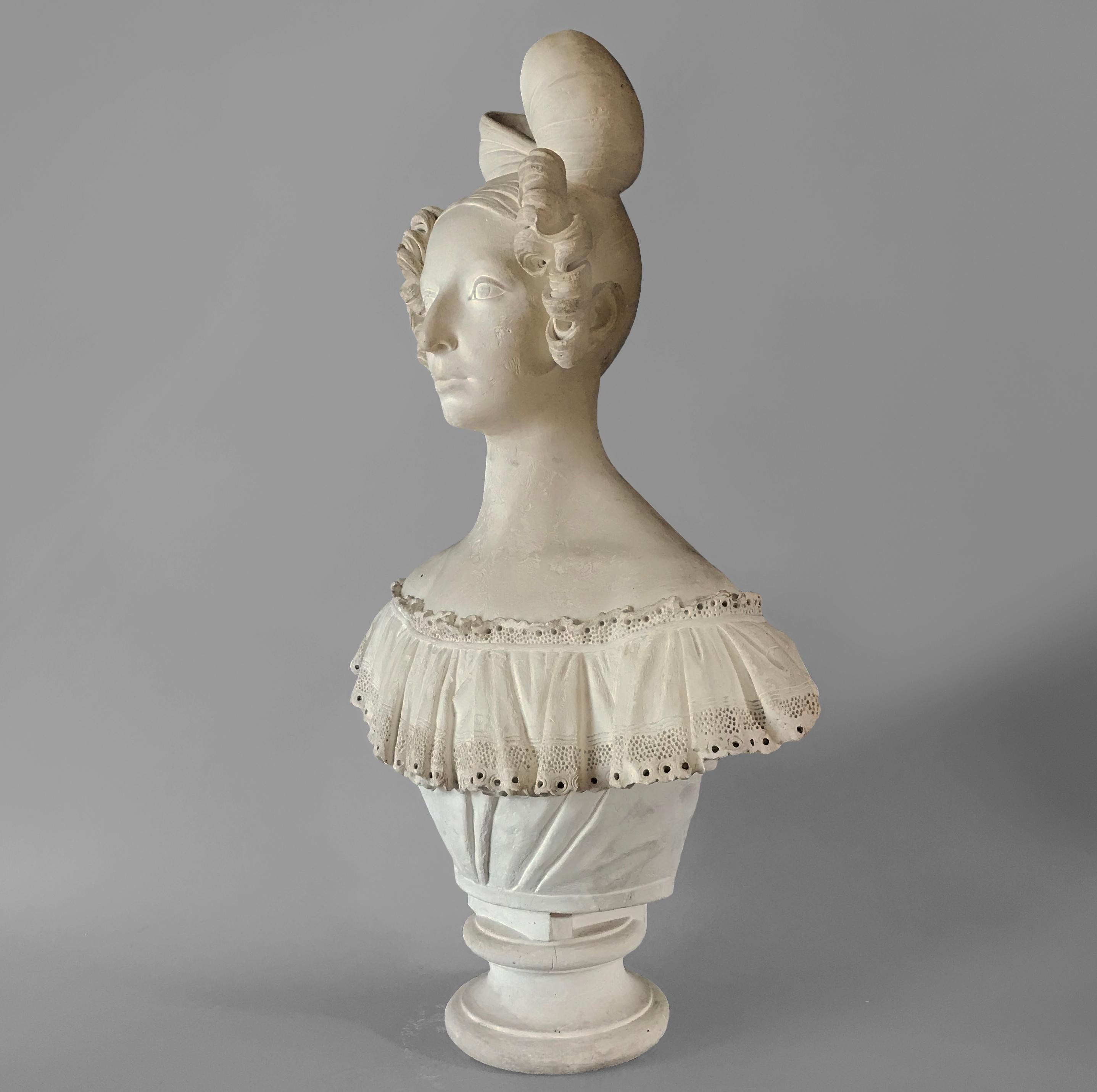 A wonderfully modelled bust of a French lady showing off her amazing coiffeured hair of curls with a large bow, wearing a gathered intricate lace top and sitting on a deeply waisted socle.