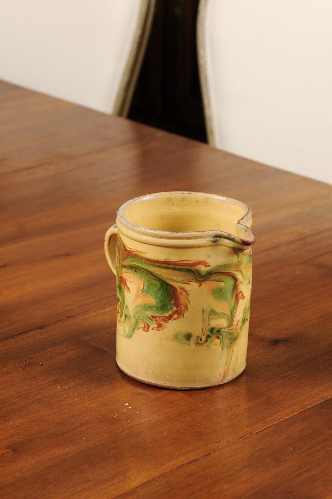 A French pottery pitcher from the 19th century, with marbleized glazed décor. Created in France during the 19th century, this rustic pottery pitcher features a soft yellow ground perfectly accented with a marbleized glazed décor showcasing russet