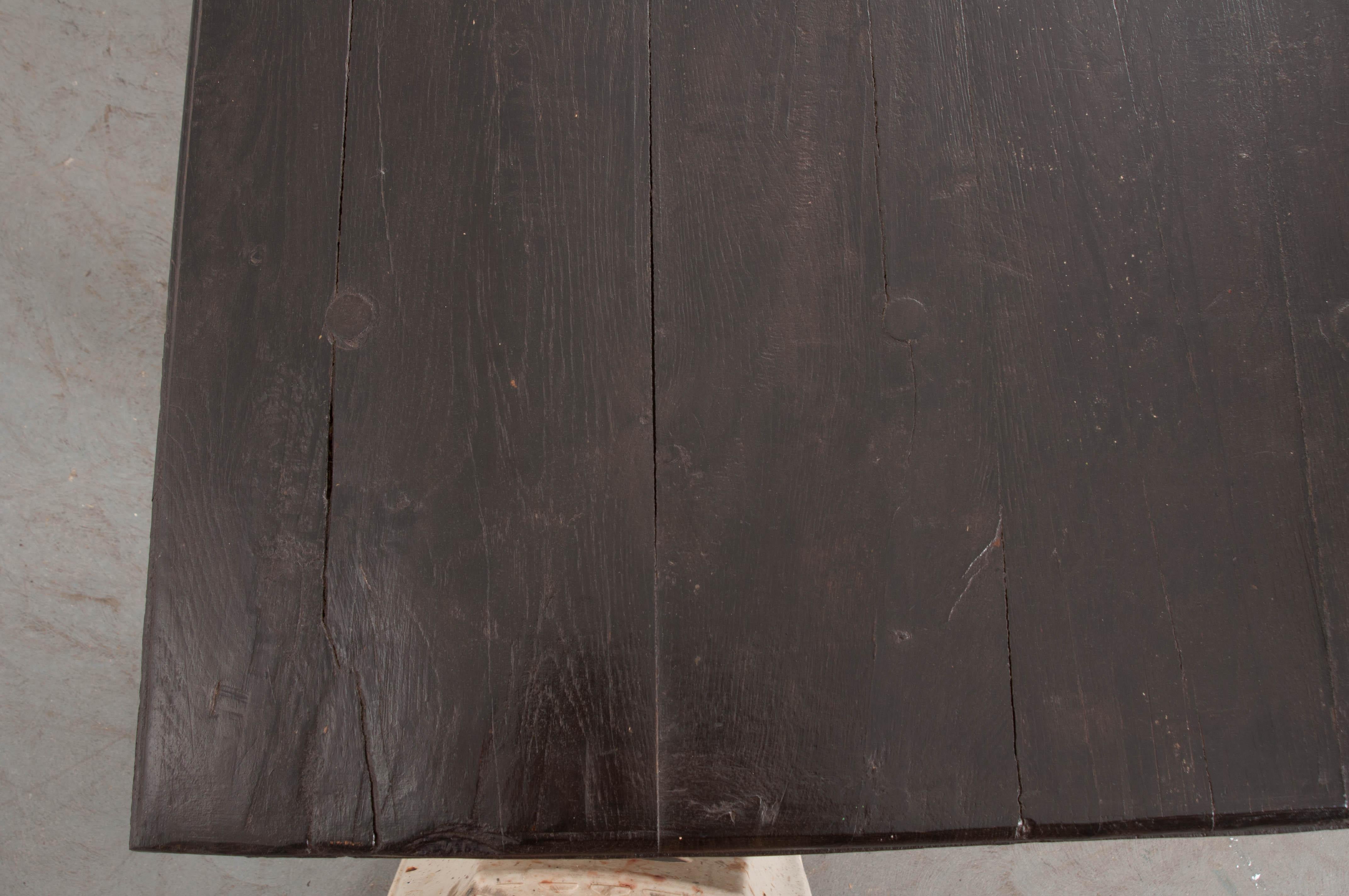 This handsome provincial trestled farm table, circa 1860s, is from France and features a deep, almost ebony, stain. Of doweled construction, the surface has some honest repairs that only add to its charm. There is plenty of leg room on each end