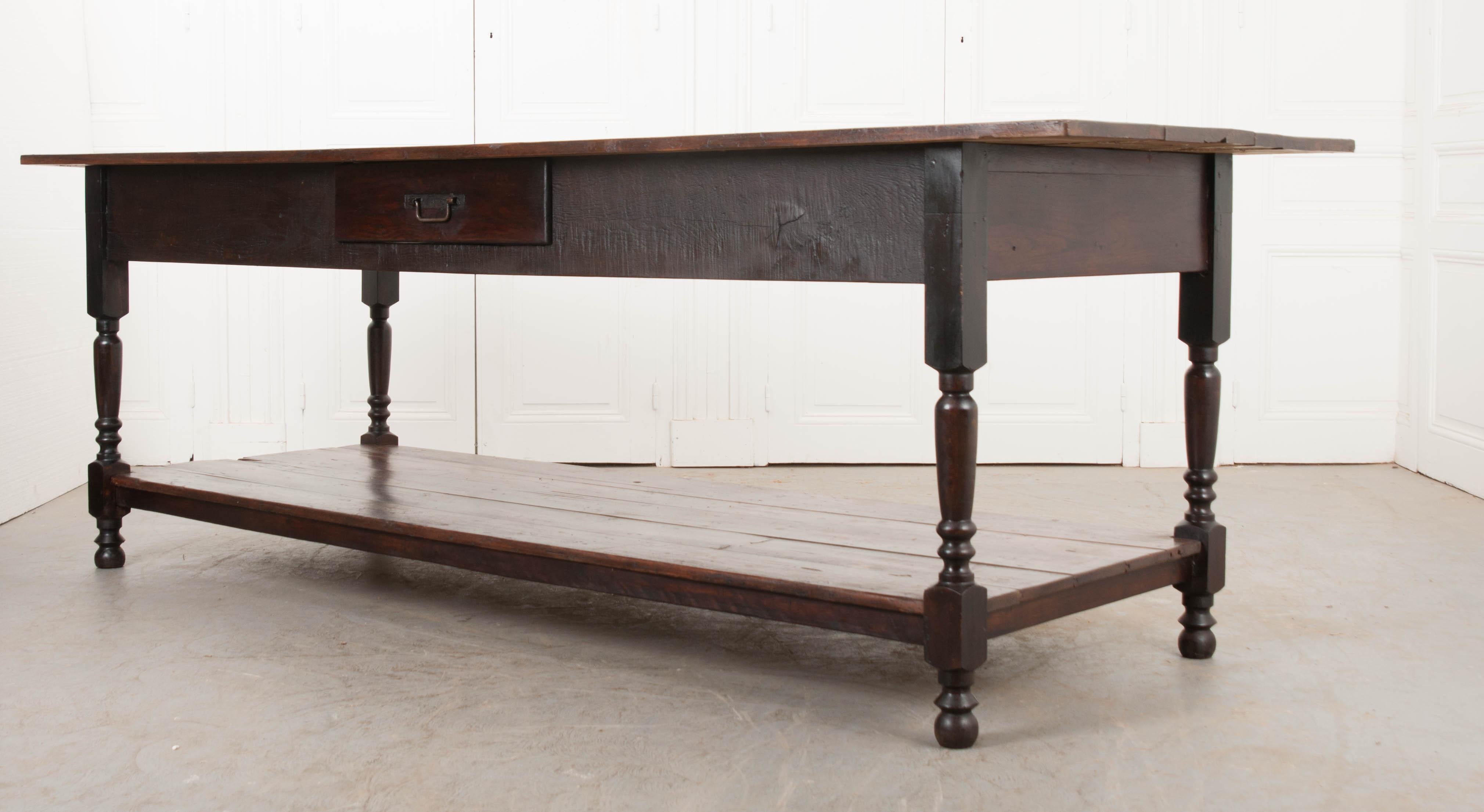 This wonderful Provincial walnut drapery table, circa 1890, is from Burgundy, France and features a plank top over an apron outfitted with a single drawer. The whole is supported on turned legs and bun feet. A roomy stretcher shelf allows for loads