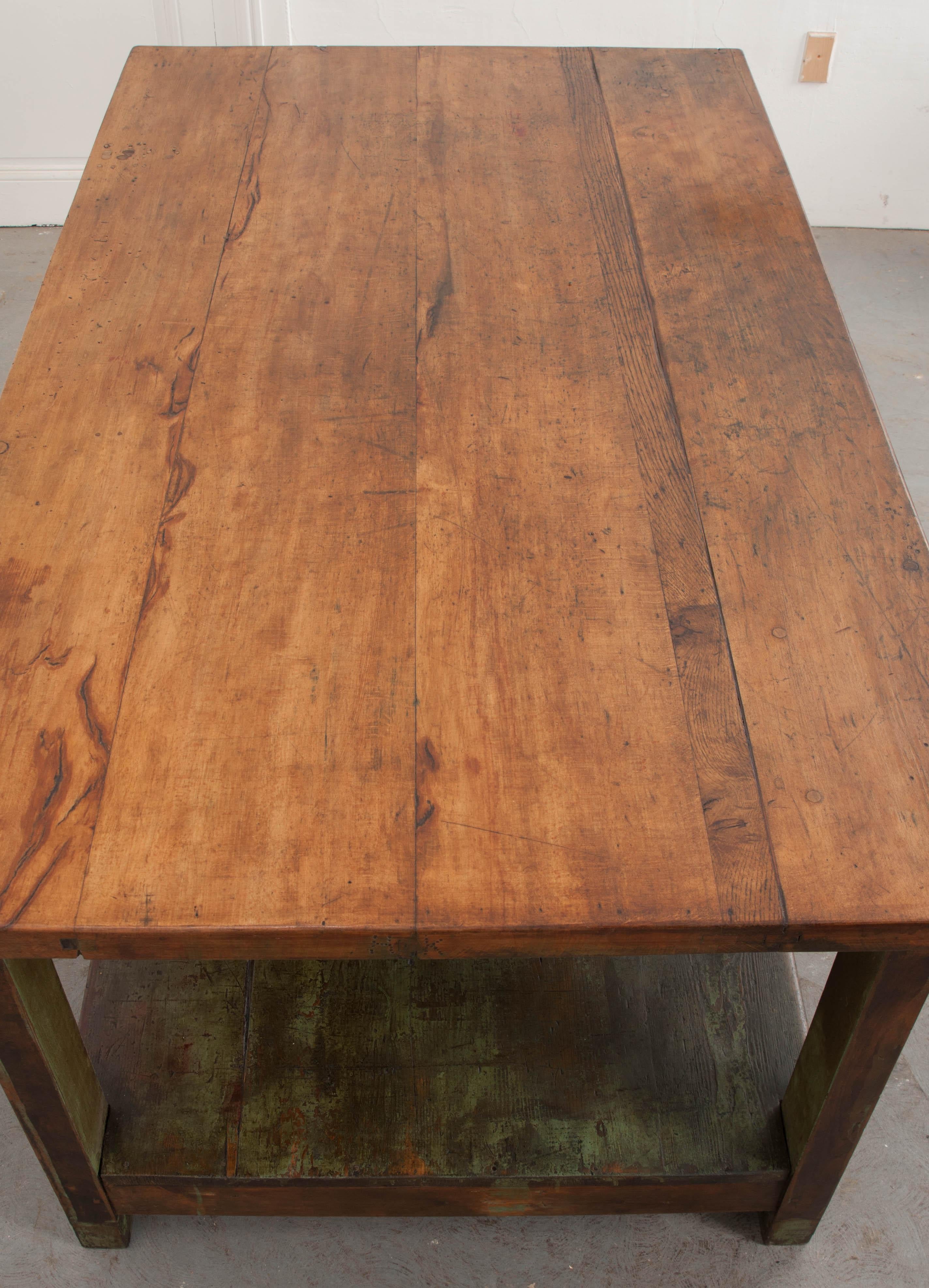 This fantastic French provincial walnut and olive-green painted work table, circa 1850s, is of weighty proportion and features a finished walnut surface of tongue-and-groove construction, over a painted base with a black-painted under-tier shelf