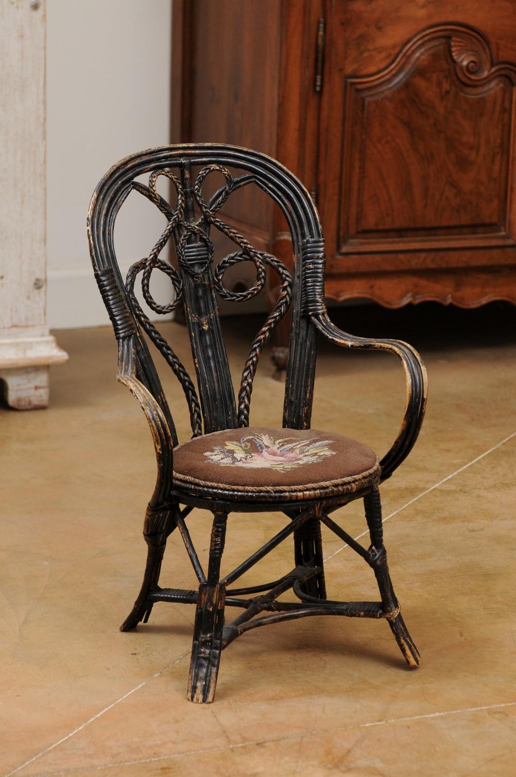 A French rattan child's chair from the 19th century, with needlepoint seat and weathered appearance. Created in France during the 19th century, this child's chair charms us with its simple lines and rustic appeal. The back, adorned with scrolling
