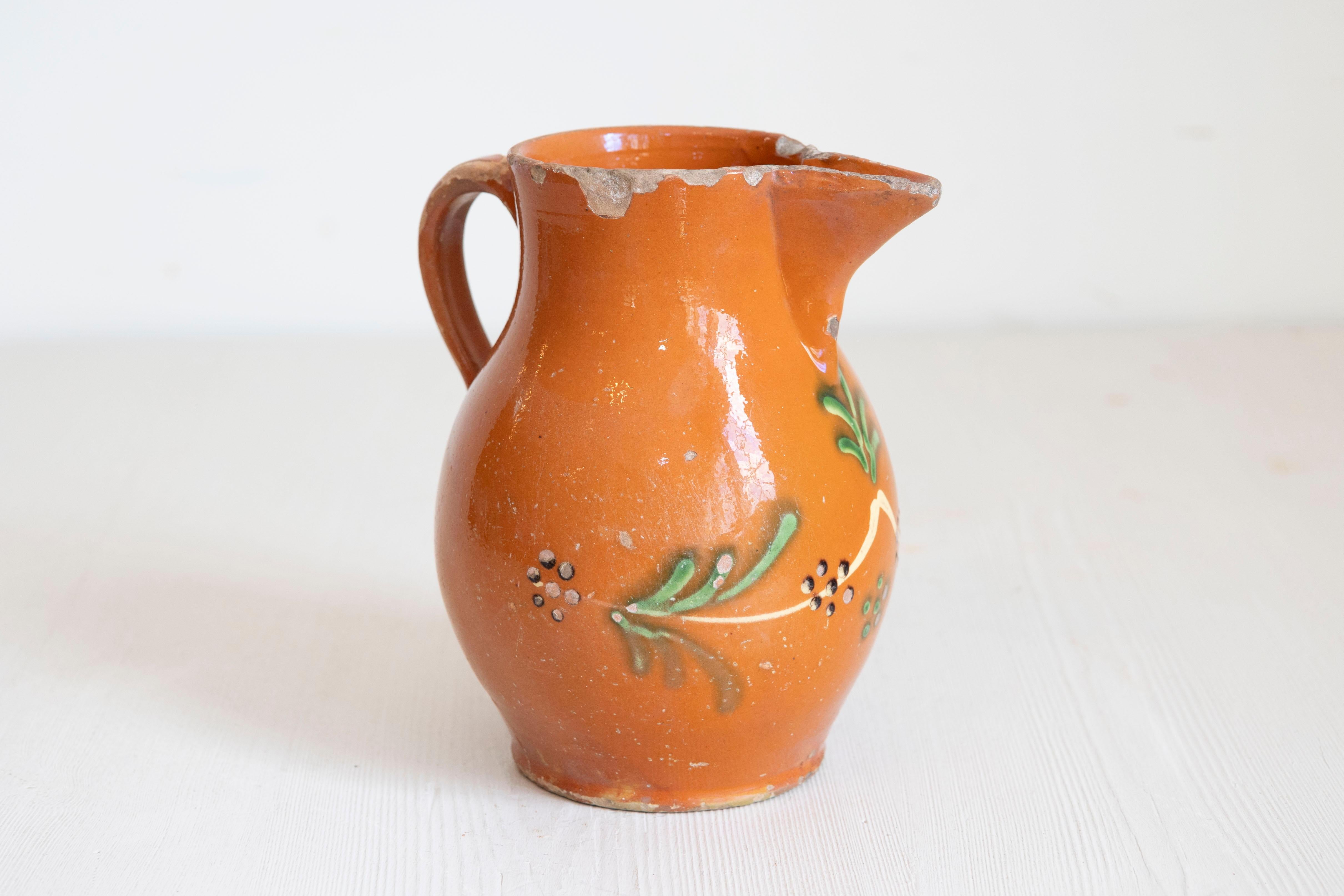 Jarra francesa de loza roja del siglo XIX, con vidriado naranja, crema y verde y motivos florales. Creada en Francia durante el siglo XIX, esta jarra de loza roja nos encanta por sus vivos colores y sus estilizados motivos florales. Esta jarra
