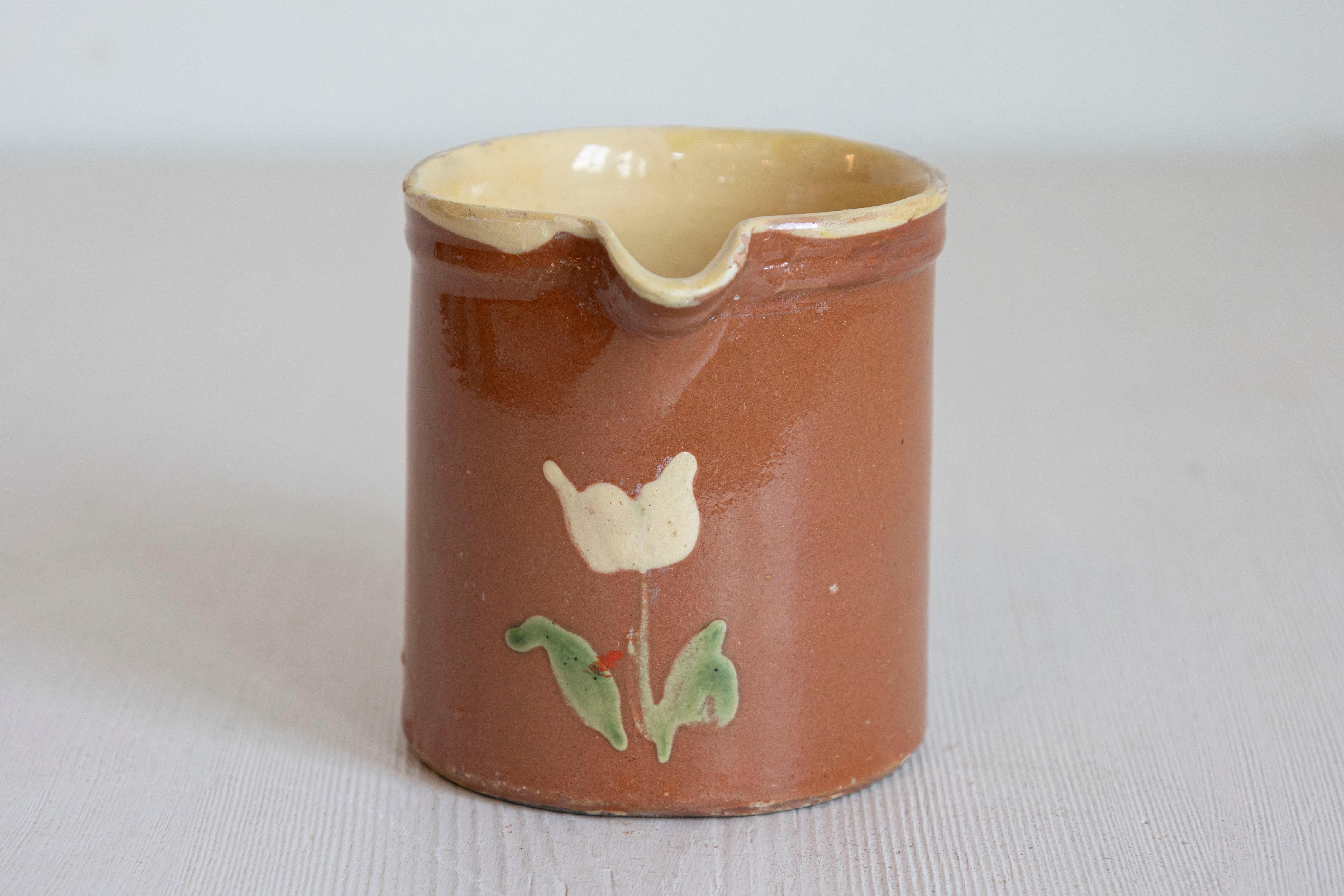 French redware pitchers from the 19th century, with white flowers, priced and sold individually $375 each. Created in France during the 19th century, each of these pitchers features a cylindrical body, adorned with a charming decor of white flowers