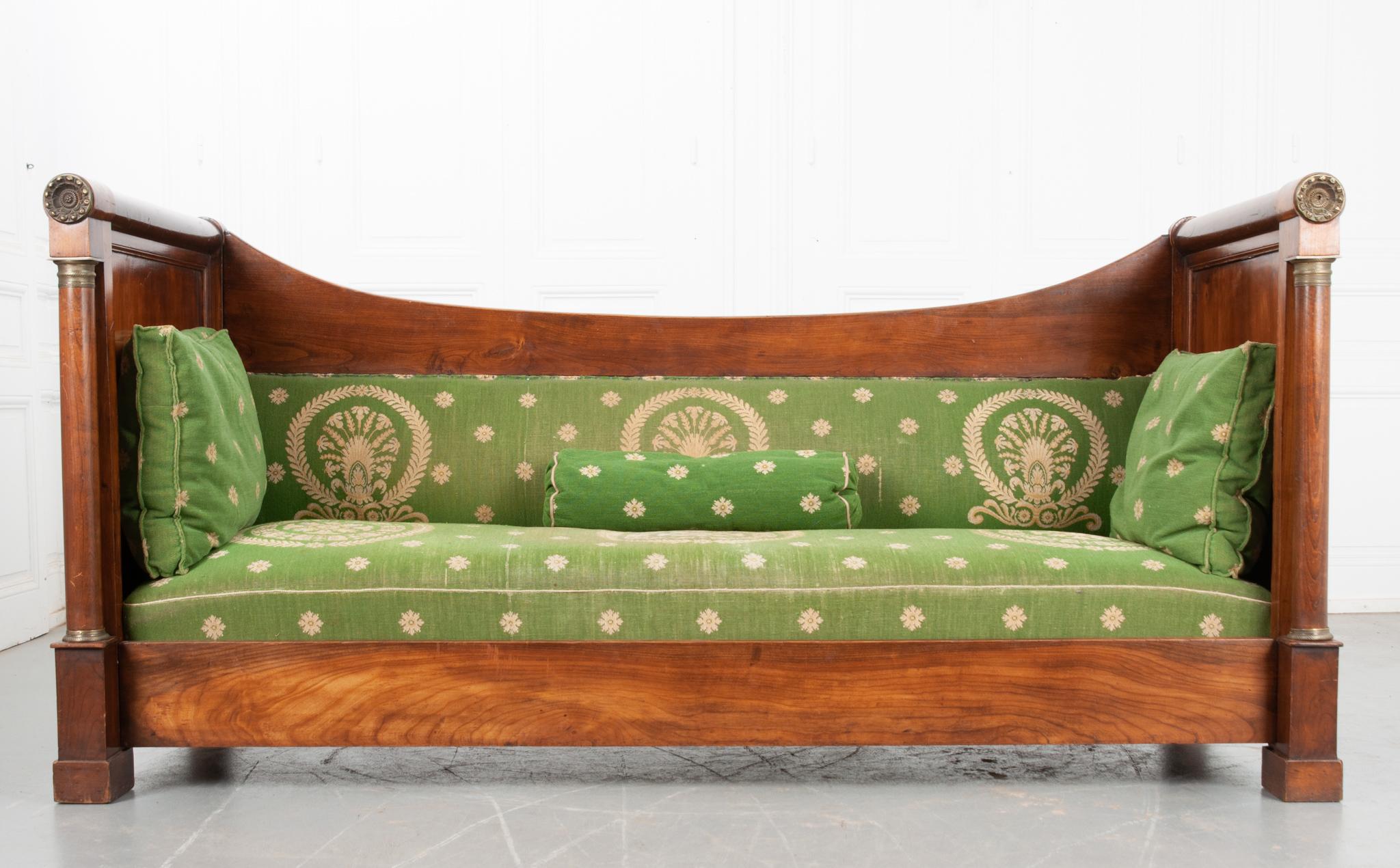 This handsome Empire style sofa is made of walnut from 19th Century France. The decorative laurel wreath and floral green upholstery is lovely against the bright wood frame. The fabric is slightly worn as one would expect with over two centuries of