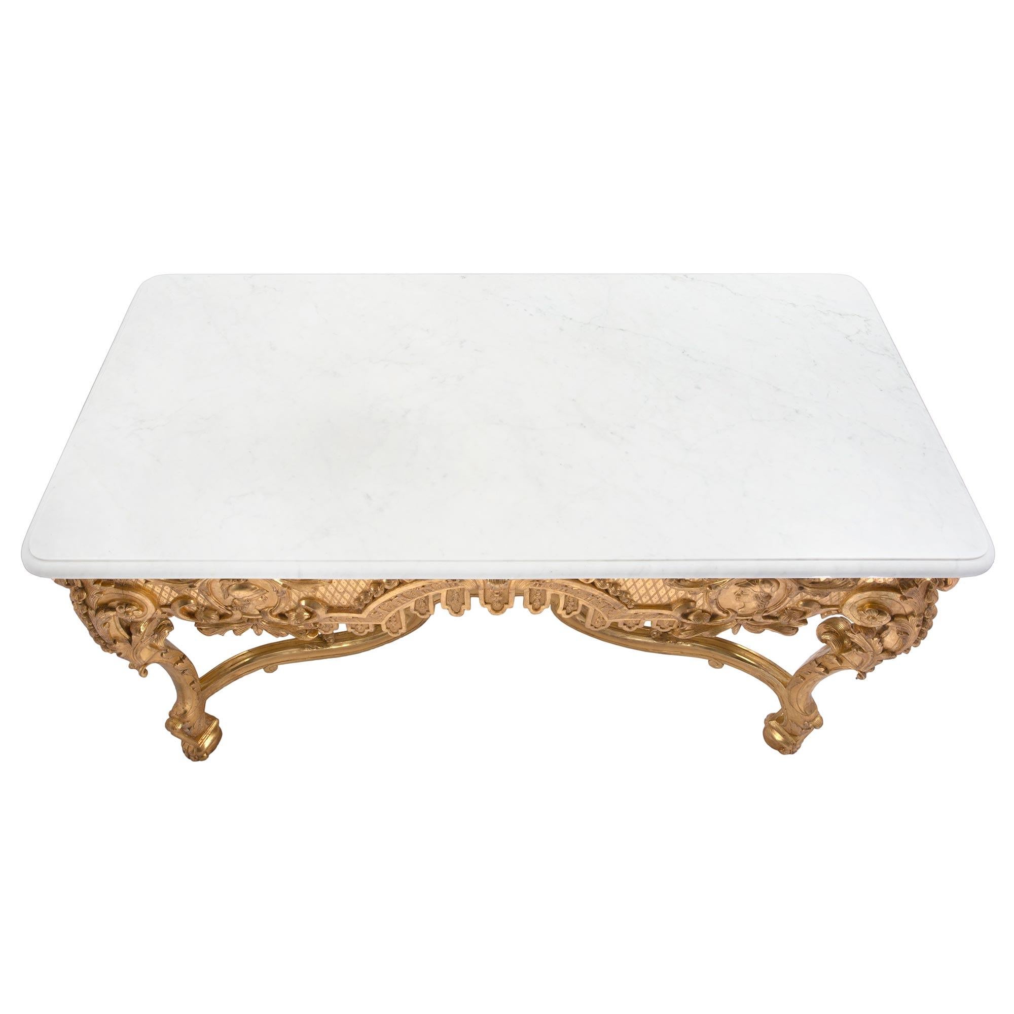 A stunning French 19th century Régence st. giltwood and white Carrara marble rectangular center table. The table is raised by handsome paw feet below impressive cabriole legs decorated with richly carved foliate designs. Each leg is connected by a