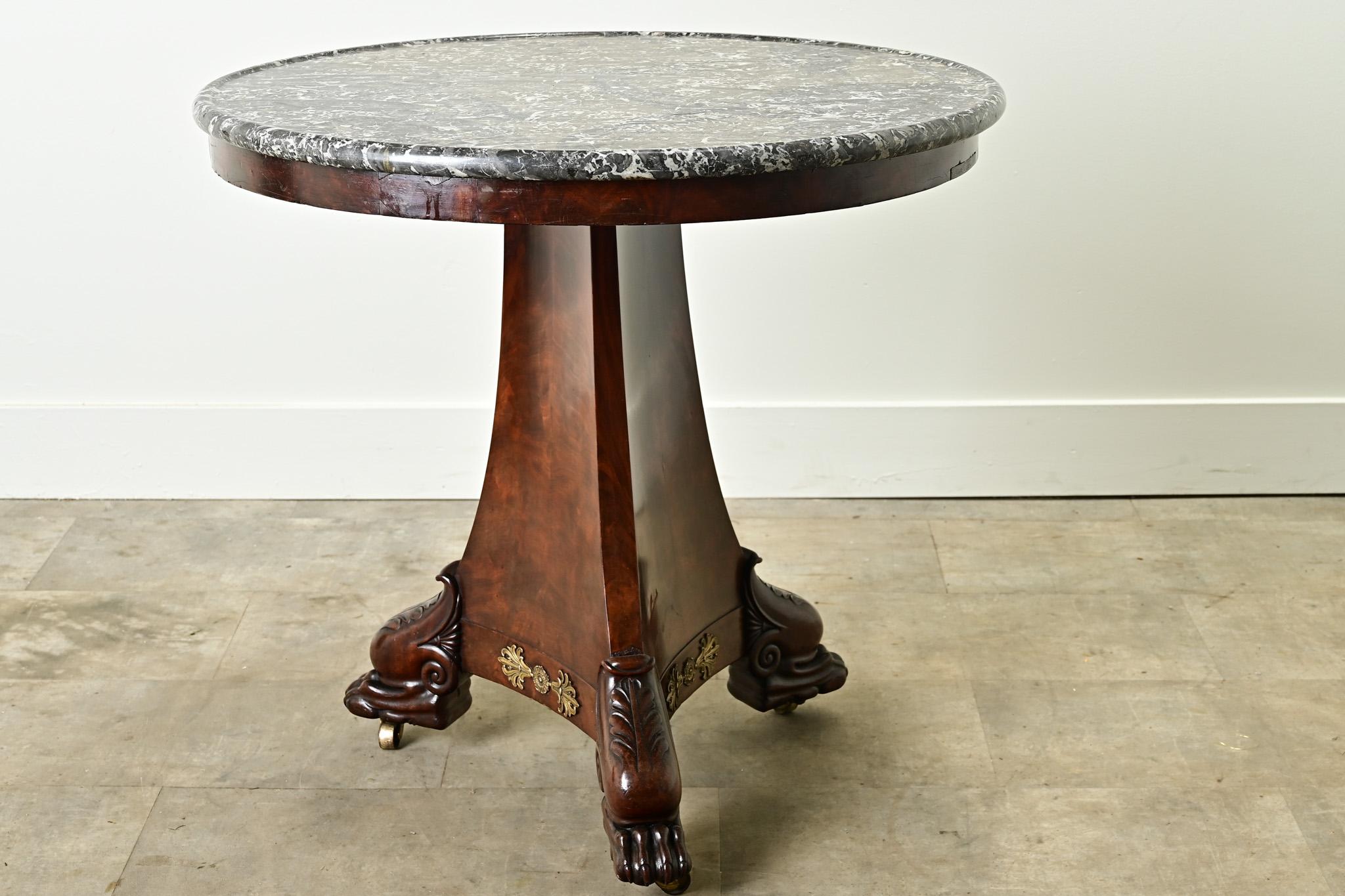 A handsome French Restauration center table made of burl mahogany. The original Saint Anne marble top rests above a three-sided concave mahogany base with gilt bronze ormolu. The original carved and decorative feet are lifted on casters. Cleaned and