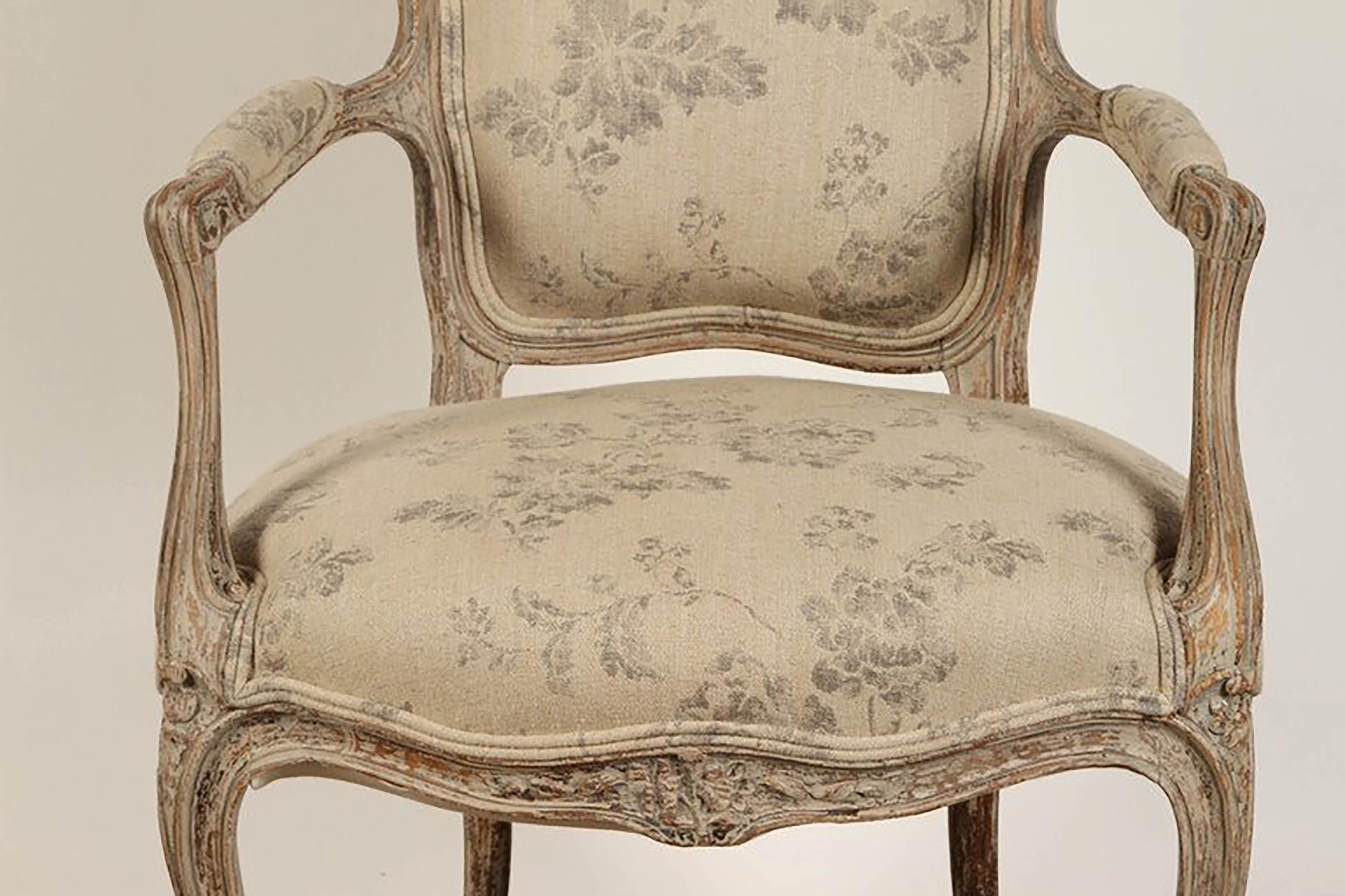 A Rococo style armchair from the 19th century, delicately carved with floral clasps to the crest and seat rails and to the tops of the cabriole legs, and scrolled arm terminals. The back, seat and arms are covered in a softly colored fabric with a