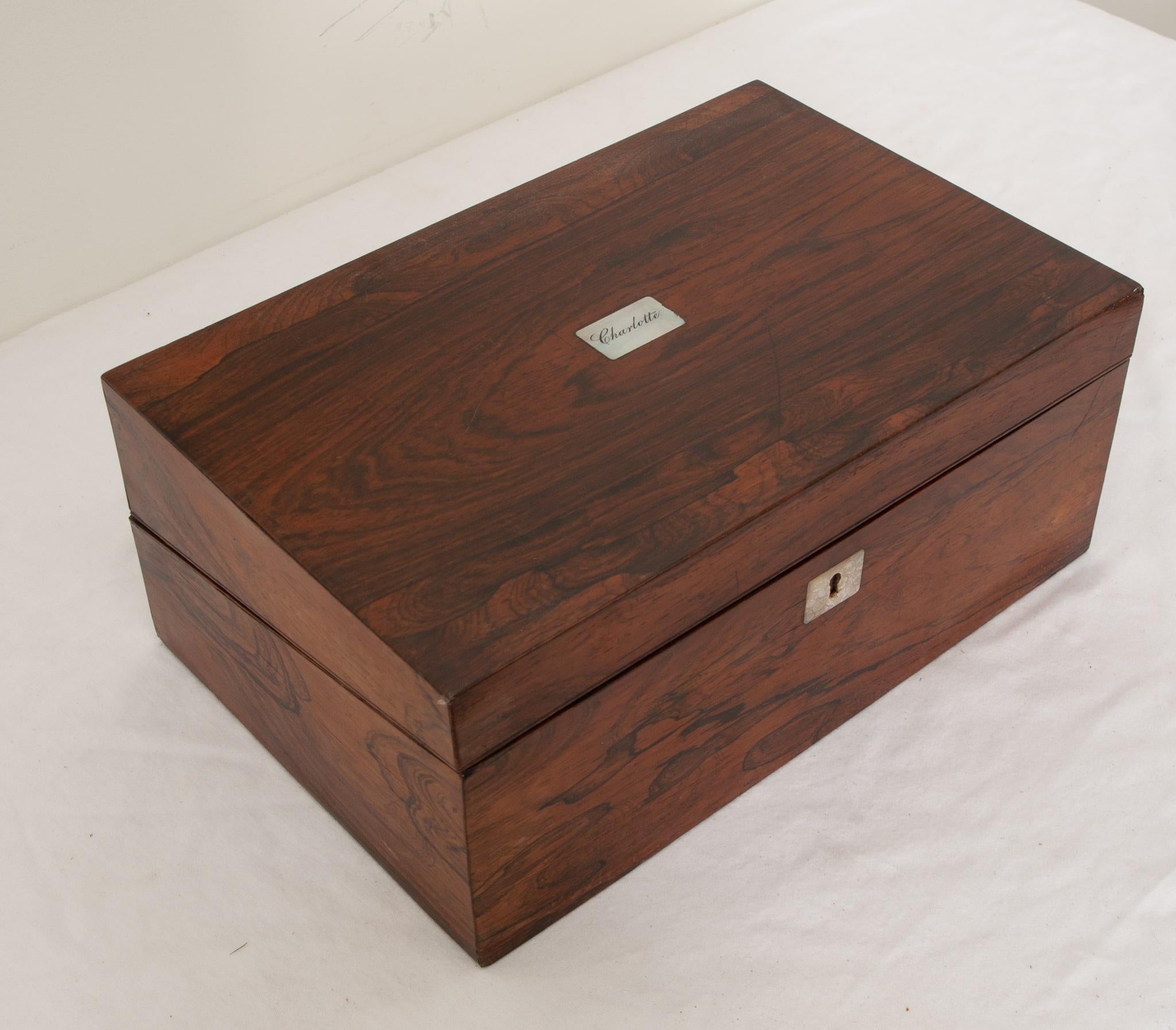 A French traveling writing box made of rosewood during the 1800’s. The top of the box is inlaid with a mother-of-pearl monogrammed “Charlotte” label. The box opens up to reveal its original sloped purple velvet writing surface. Within the box there