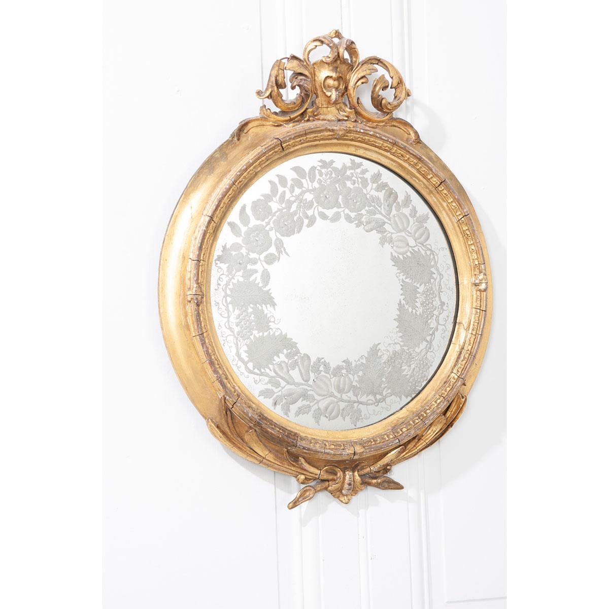 A French 19th century round gold gilt mirror, with original engraved mirror plate. The plate features flowers, fruit, leaves, and curled tendrils that have been artfully etched into the glass. The frame is adorned with intricate carvings across the