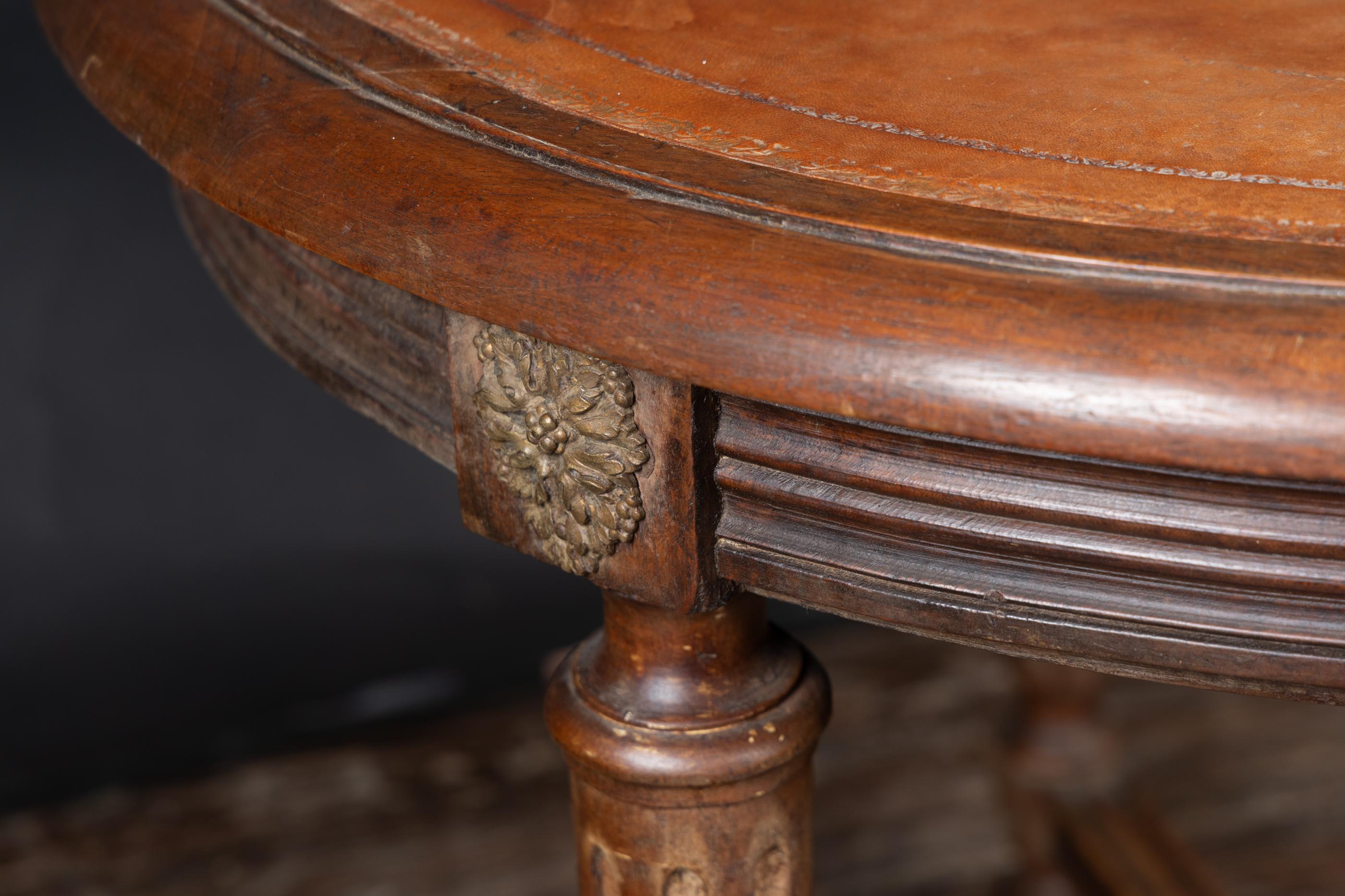 This beautiful circular mahogany table features a beautiful stretcher designed in the Louis XVI manner, and is supported by three fluted wooden legs. Dating back to the 19th century, the French antique piece sports a gold tooled leather top. The