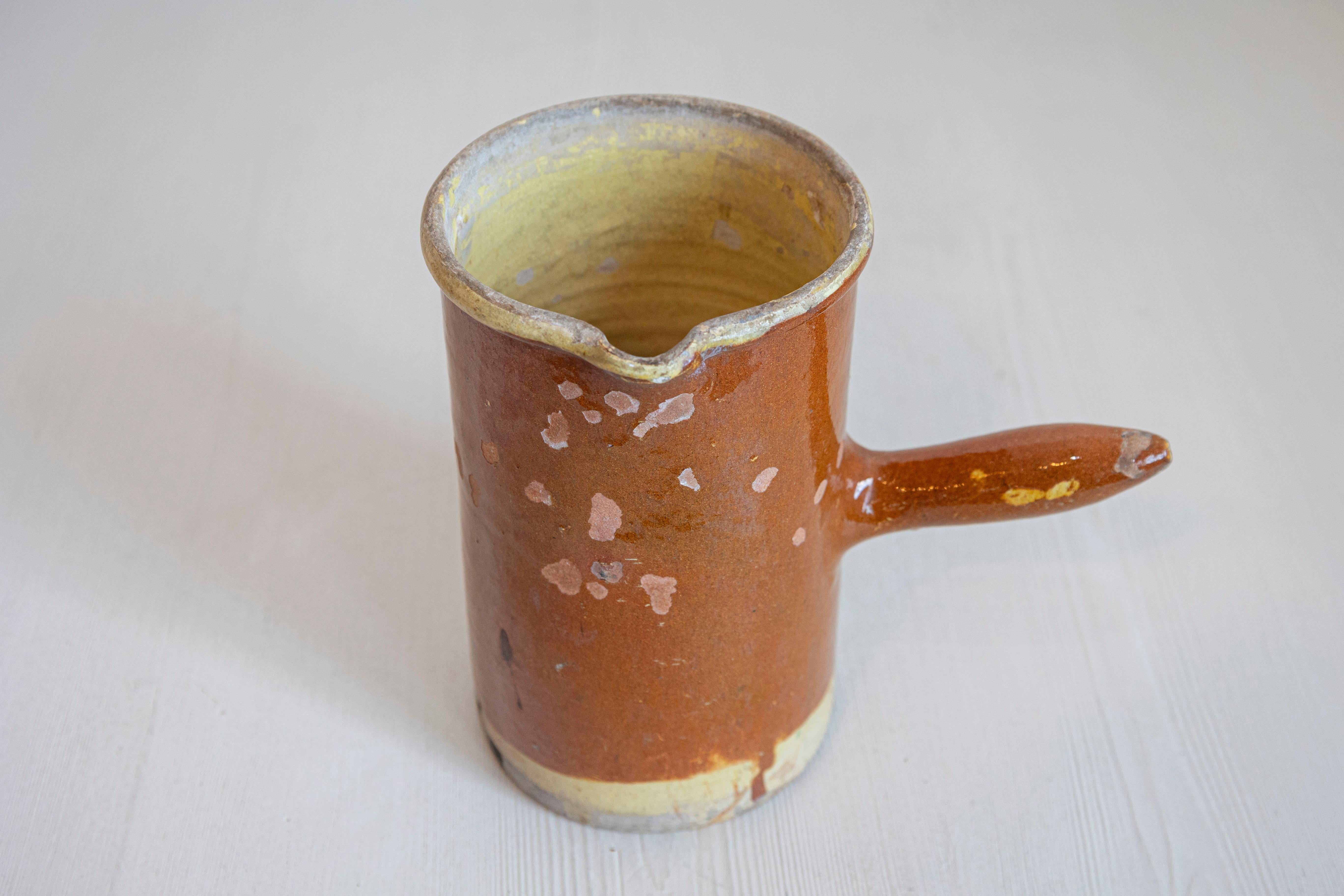A French rustic pitcher from the 19th century, with rust colored glaze and straight handle. Created in France during the 19th century, this pitcher features a cylindrical body adorned with a rust ground showing a nicely weathered appearance.